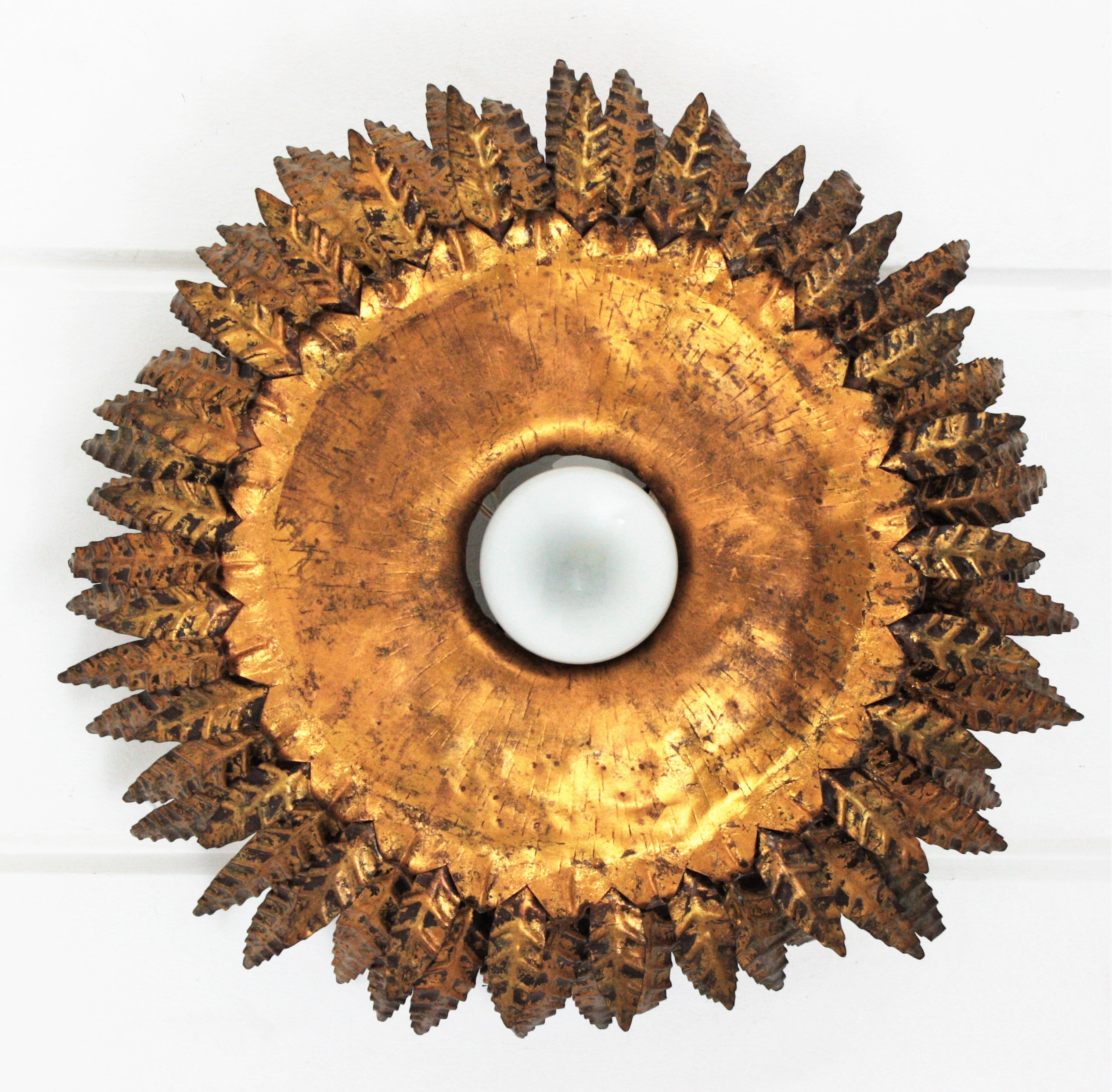 Outstanding triple layered sunburst ceiling flush mount in gold gilt iron. Spain, 1950s.
This sunburst flushmount was entirely made by hand. It has a beautiful Brutalist design with handcut details and three layers of hammered and gilded iron leaves