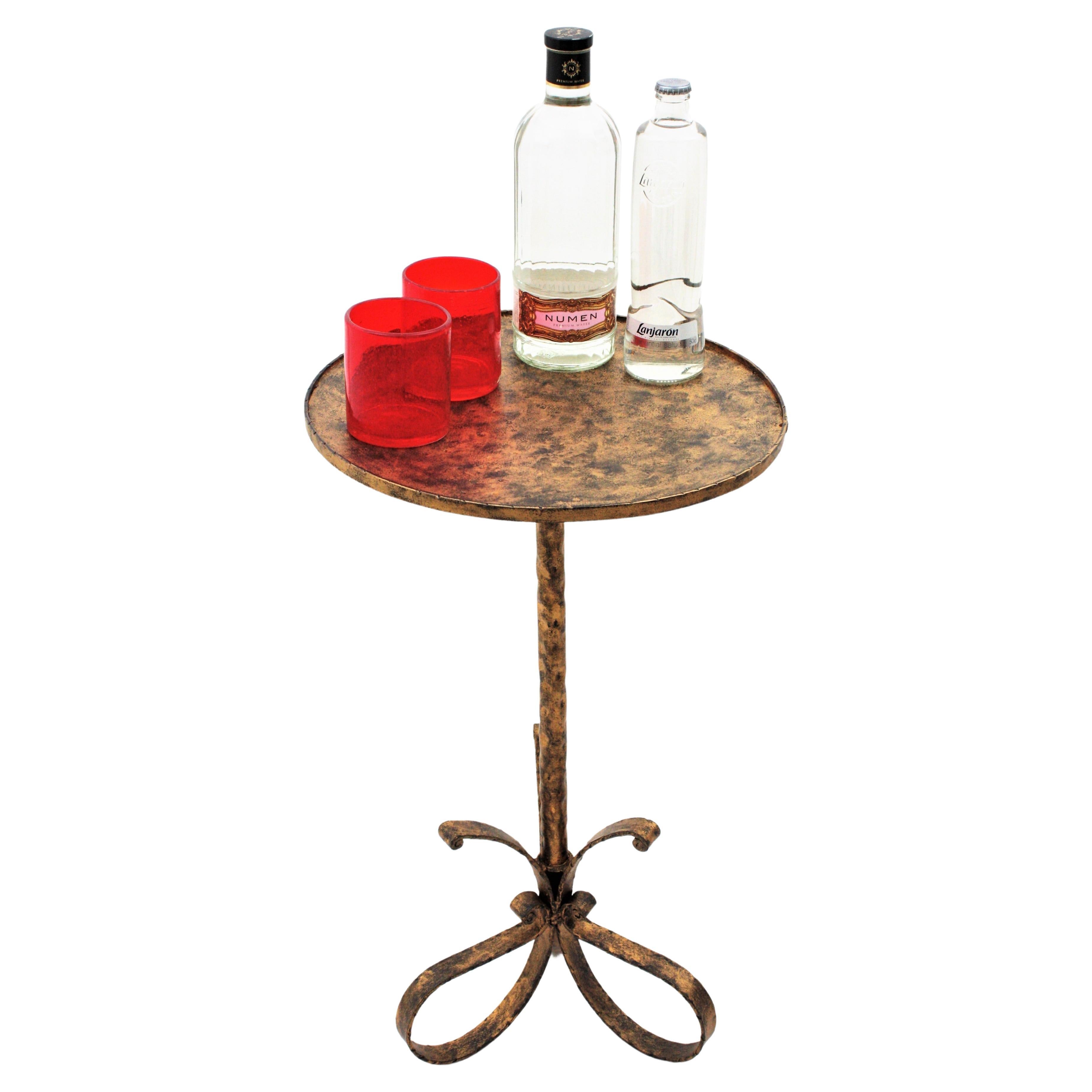 Lovely hand-hammered gilt patinated occasional table or martini table with three-footed looped base, Spain, 1940-1950s.
The top is large enough to be used as a coffee table and stands up on a loop shaped iron base adorned with scroll endings.
Use it