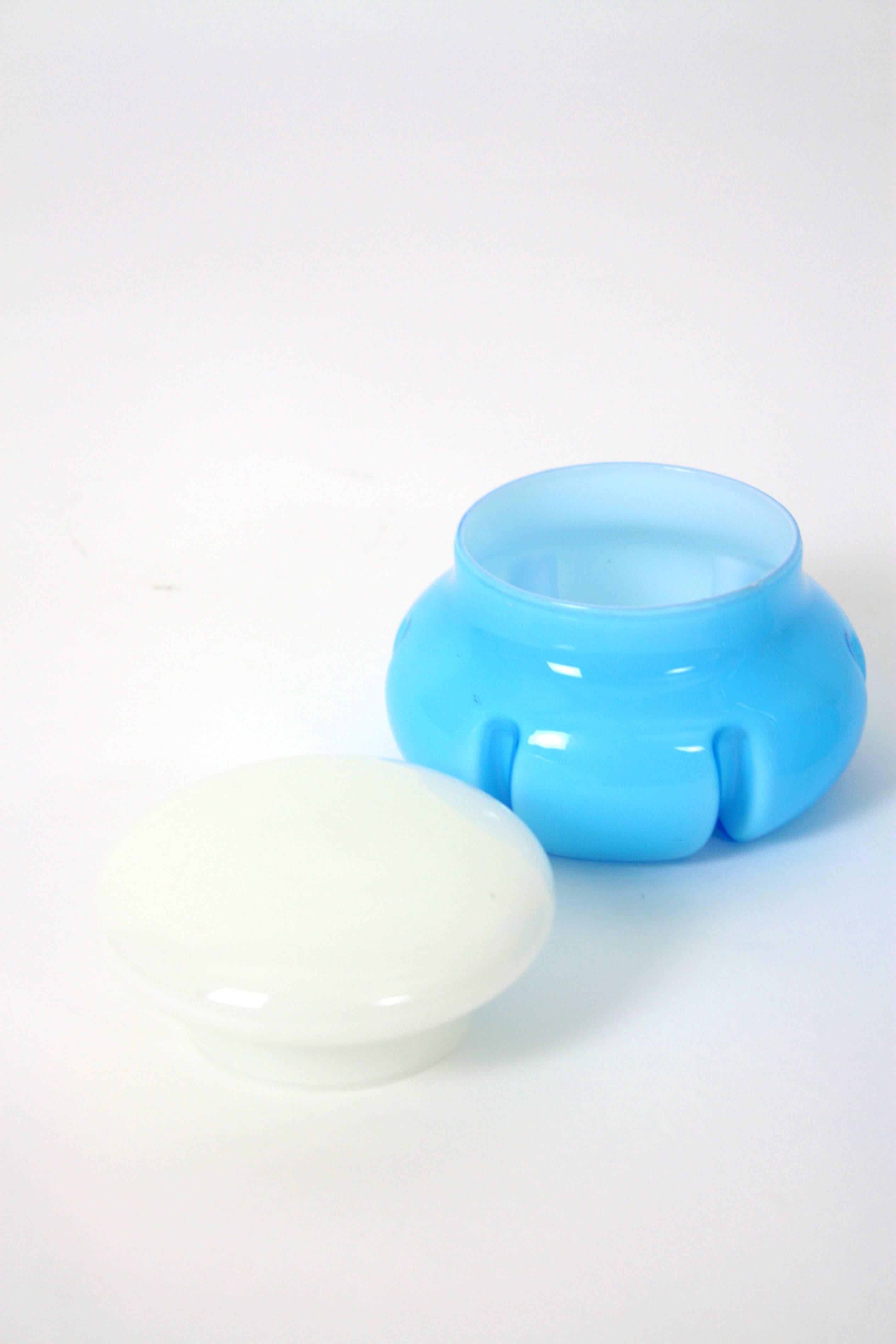Juego de decantador y caja con tapa Vanity Set.
Un vistoso tocador de cristal soplado Empoli de la Era Espacial. Italia años 60.
El conjunto se compone de un decantador de perfume de cristal azul bebé con tapón blanco y un recipiente o caja de