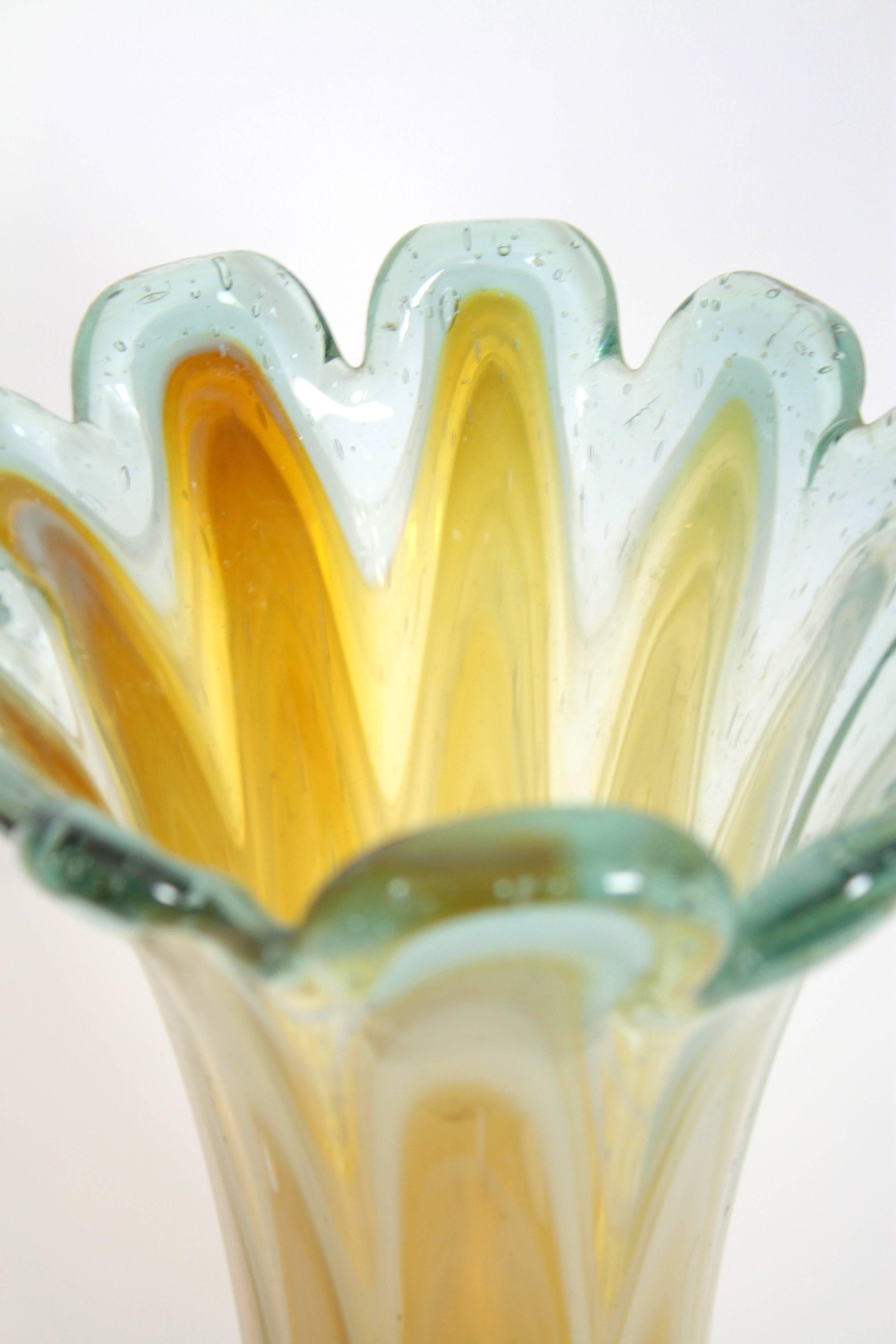 Skulpturale Vase aus mundgeblasenem Murano-Glas mit Wellenschliff (bernsteinfarbenes, cremefarbenes und weißes Glas), eingefasst in Klarglas. Italien, 1960er Jahre.
Die Vase ist in ausgezeichnetem Zustand. 
Punktförmige Markierung darunter.
Zu