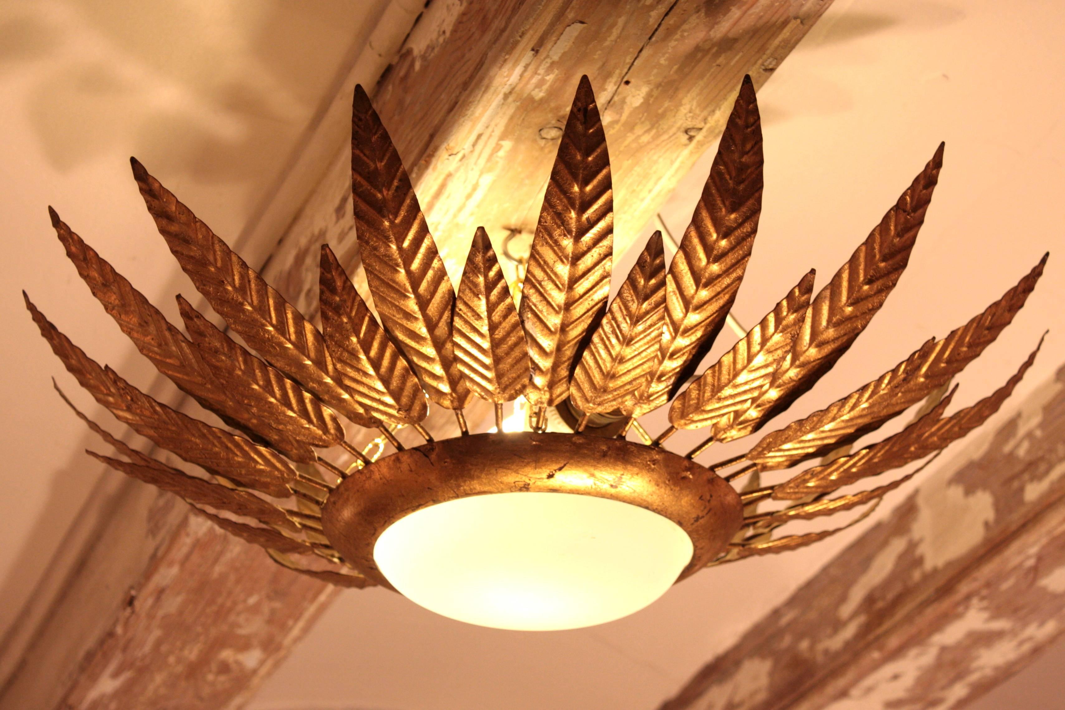 Beautiful gilt iron sunburst flush mount in the style of Hollywood Regency framed with leaves in two sizes. It wears its original opaline glass that creates a softened light and it has gold leaf finish.
Spain, 1950-1960s.