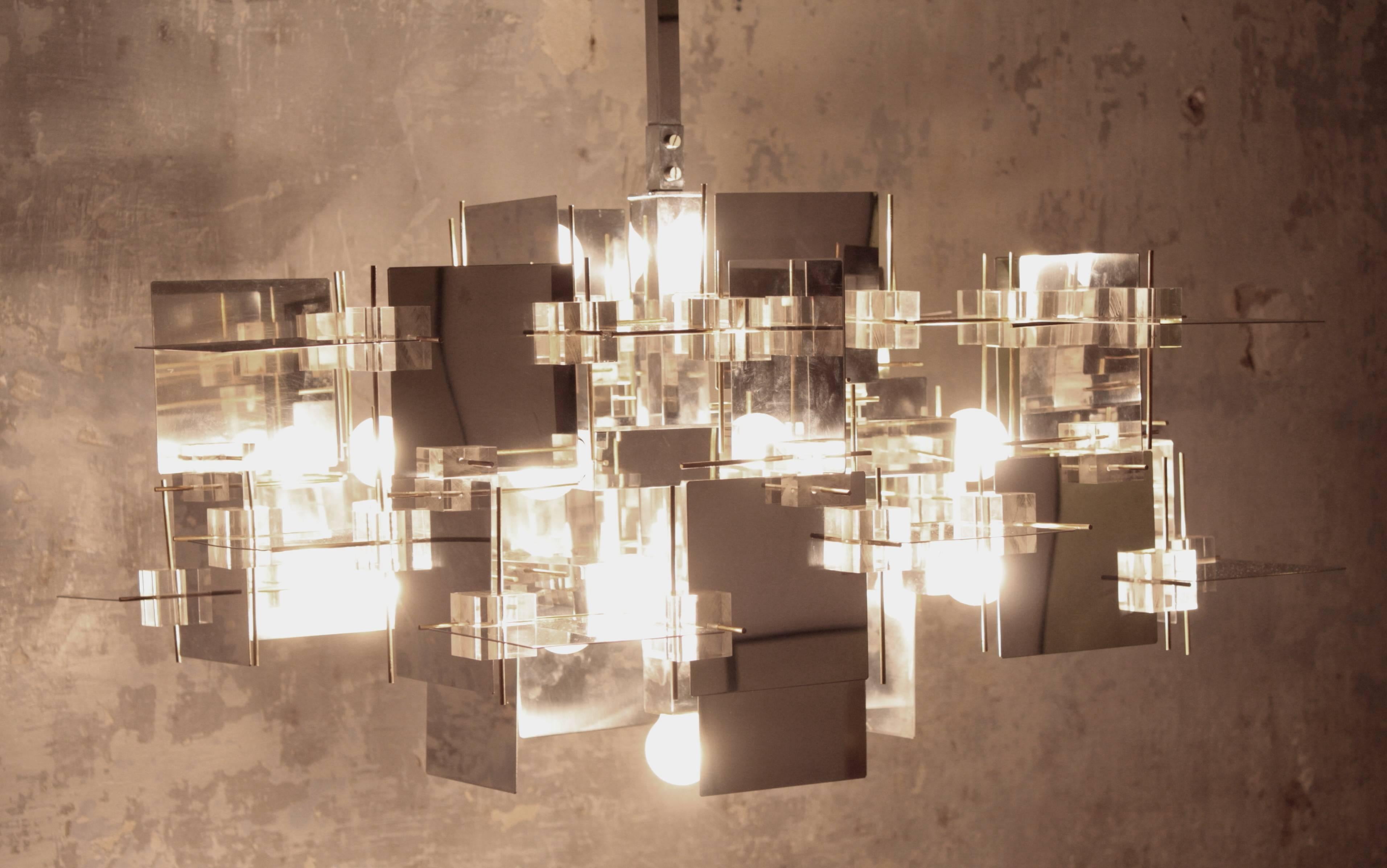 Spectacular multi-dimensional constructivist chandelier designed by Gaetano Sciolari. The chandelier is composed by polished chrome steel panels at varying axis with Lucite geometric cubes and brass pin accents and it has 13 sockets.
The design of