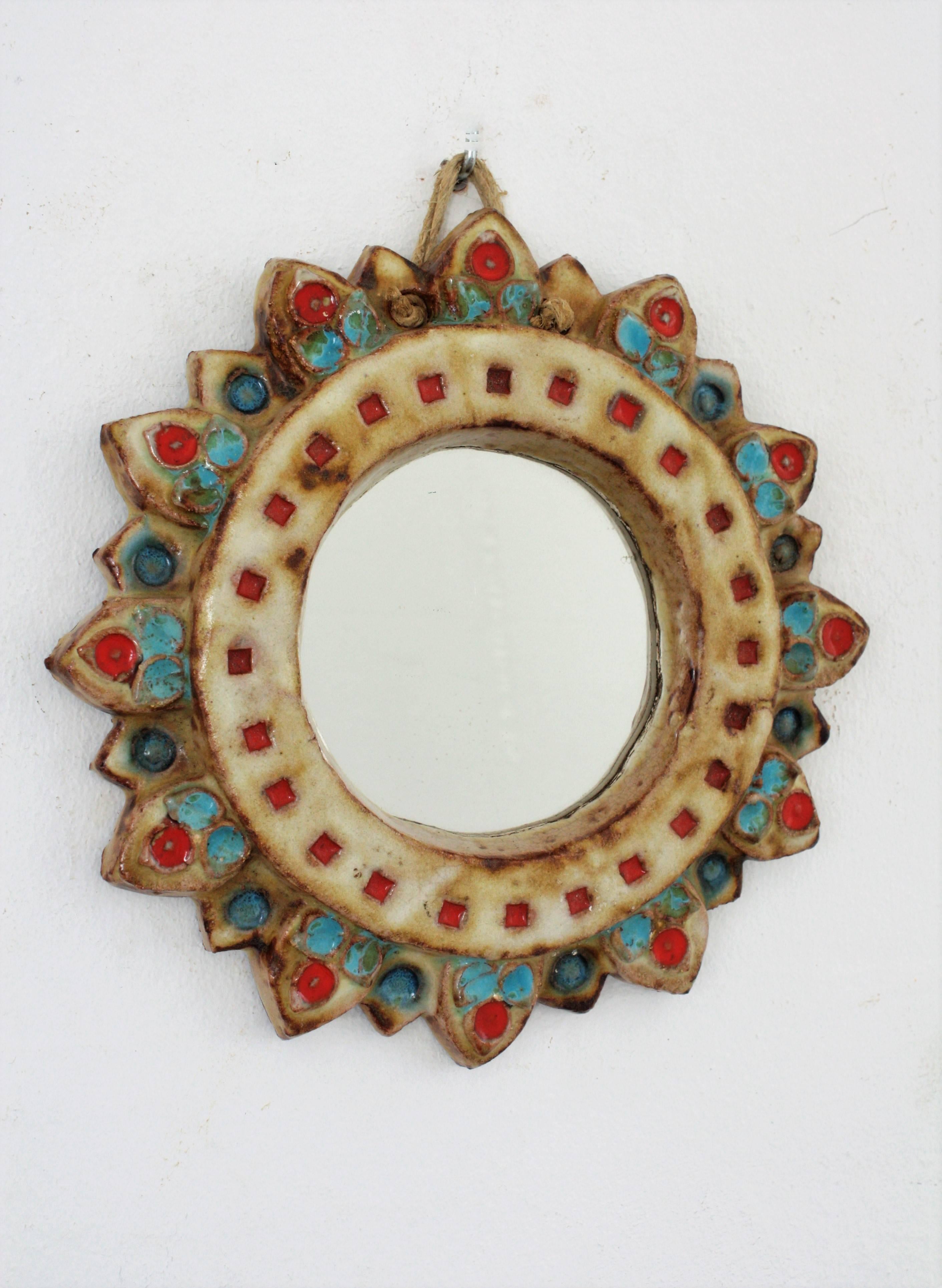 A colorful glazed ceramic sunburst mirror in ivory color with colorful blue, green and red accents from La Roue-Vallauris in the manner of Georges Pelletier. 
Signed La Roue on the back.
France, 1950s.