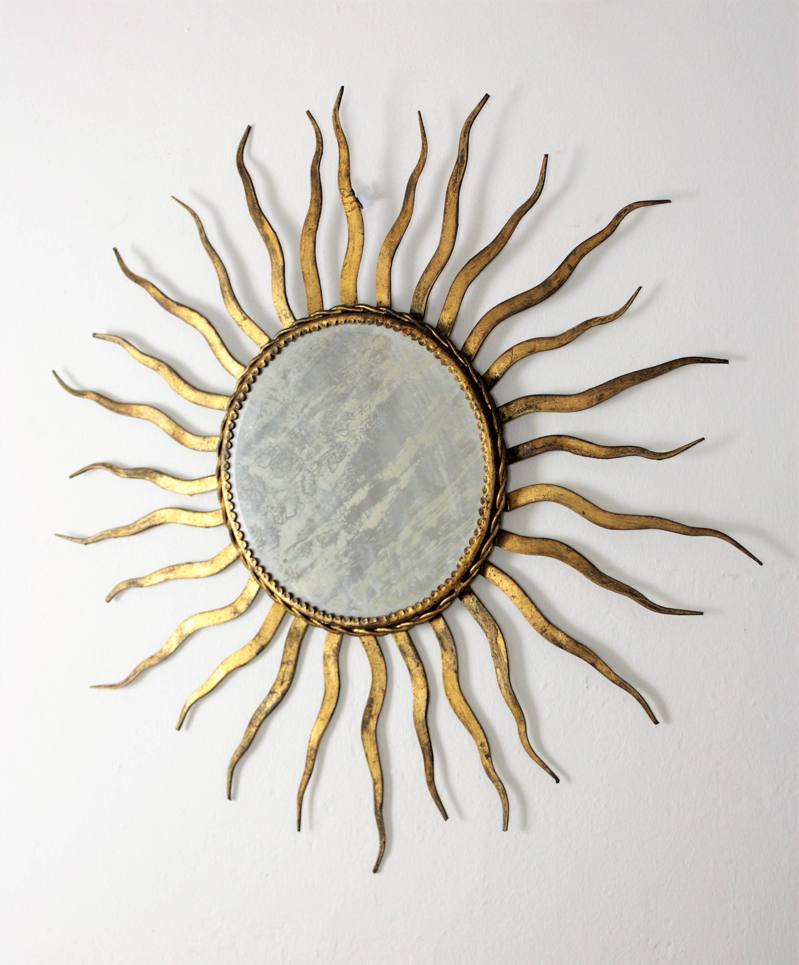 Hand-hammered iron sunburst mirror with original vintage patina in gold leaf finish. This mirror wears its original beveled glass and has all the taste of the Gilbert Poillerat style.
France, 1950s-1960s.
A beautiful piece to place alone or in a