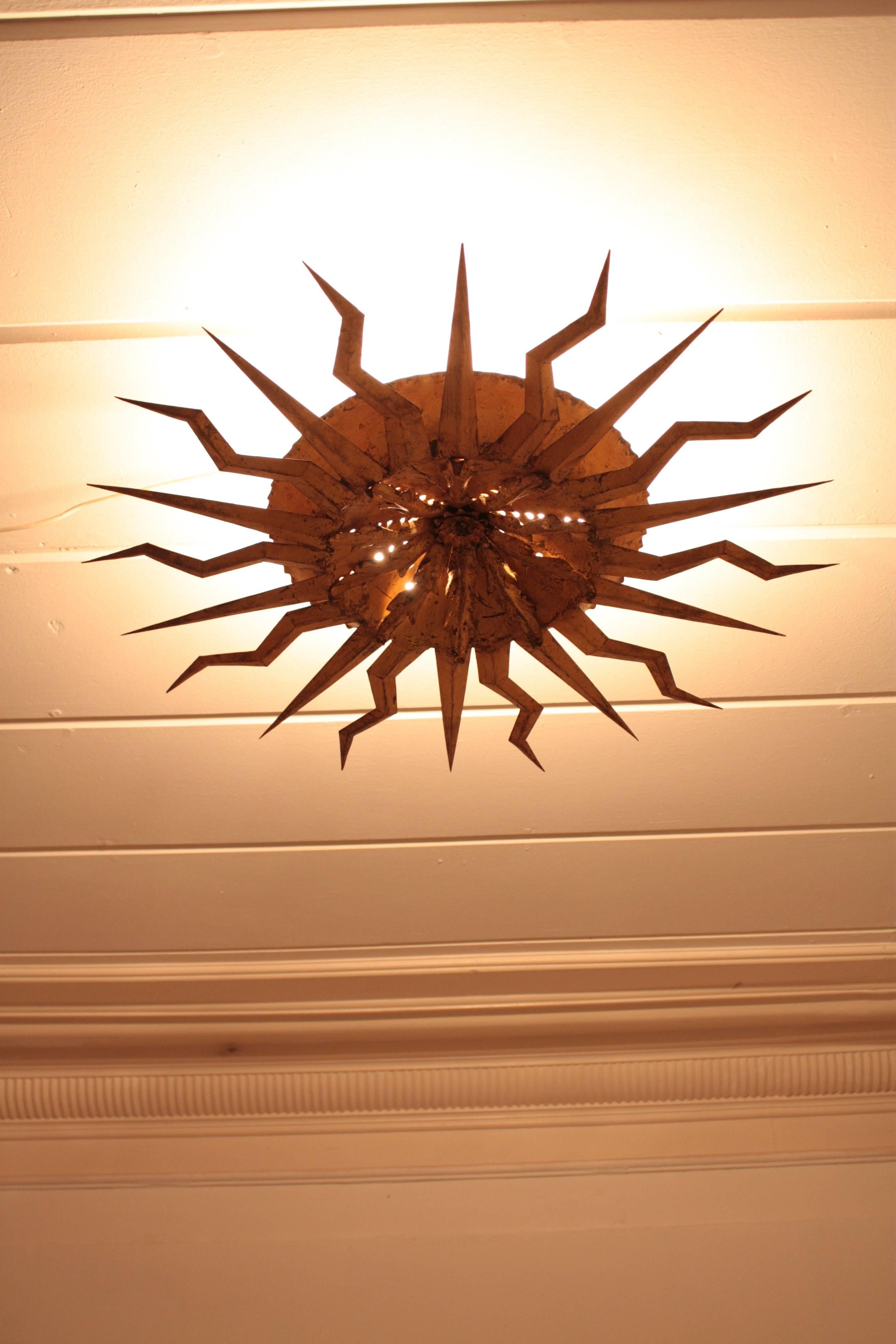 Spectacular three lights hand-hammered gilt iron starburst or sunburst ceiling fixture with flowerburst decoration in the center of the piece. This flush mount was handcrafted in Spain at the fifties, it has gold leaf finish and a beautiful original