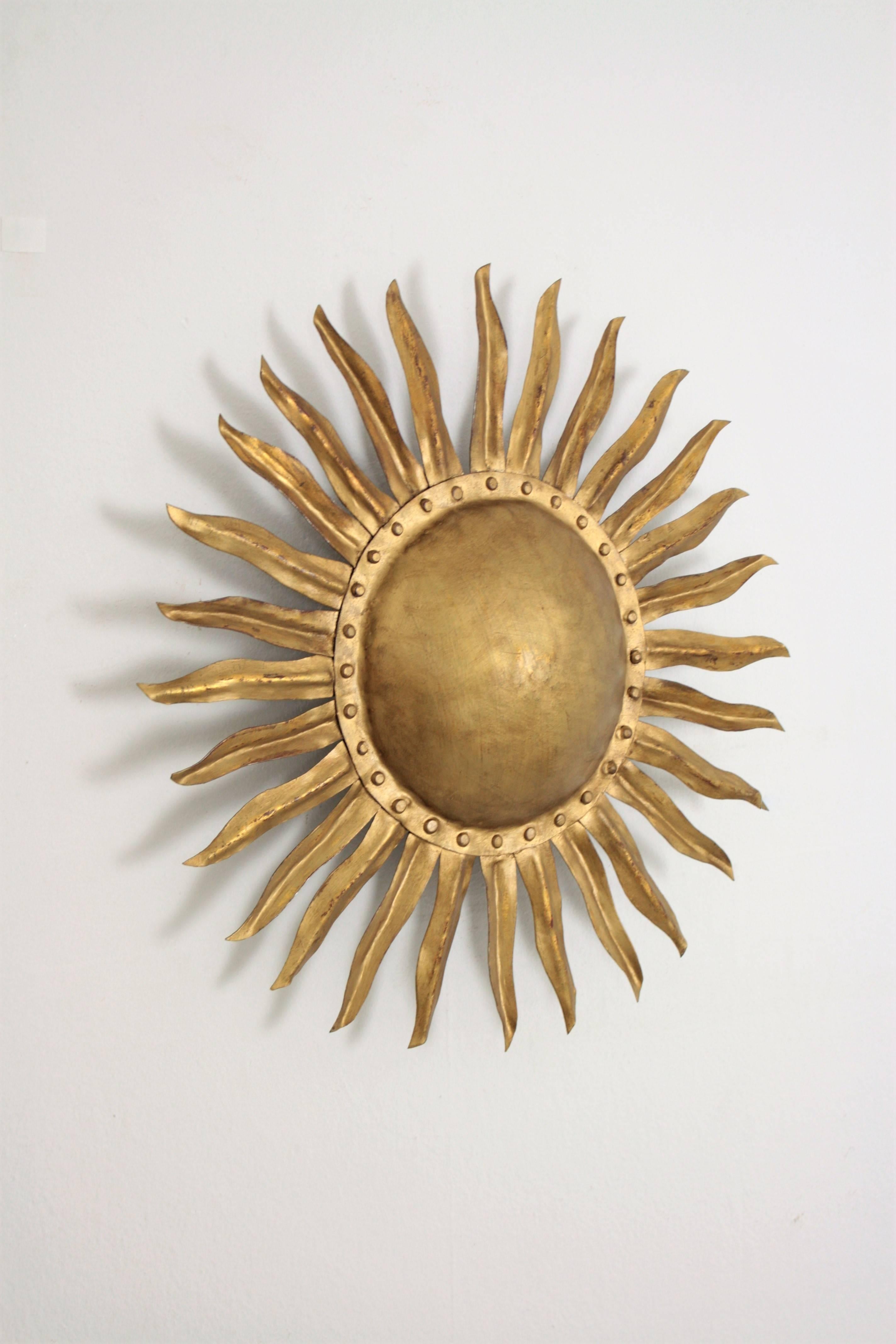 Unique hand-hammered gilt iron sunburst wall decoration or light fixture. Beautiful detail of nails surrounding the central sphere.
A highly decorative piece placed alone but also beautiful placed with other sunburst mirrors. Spain, 1940s.

Follow