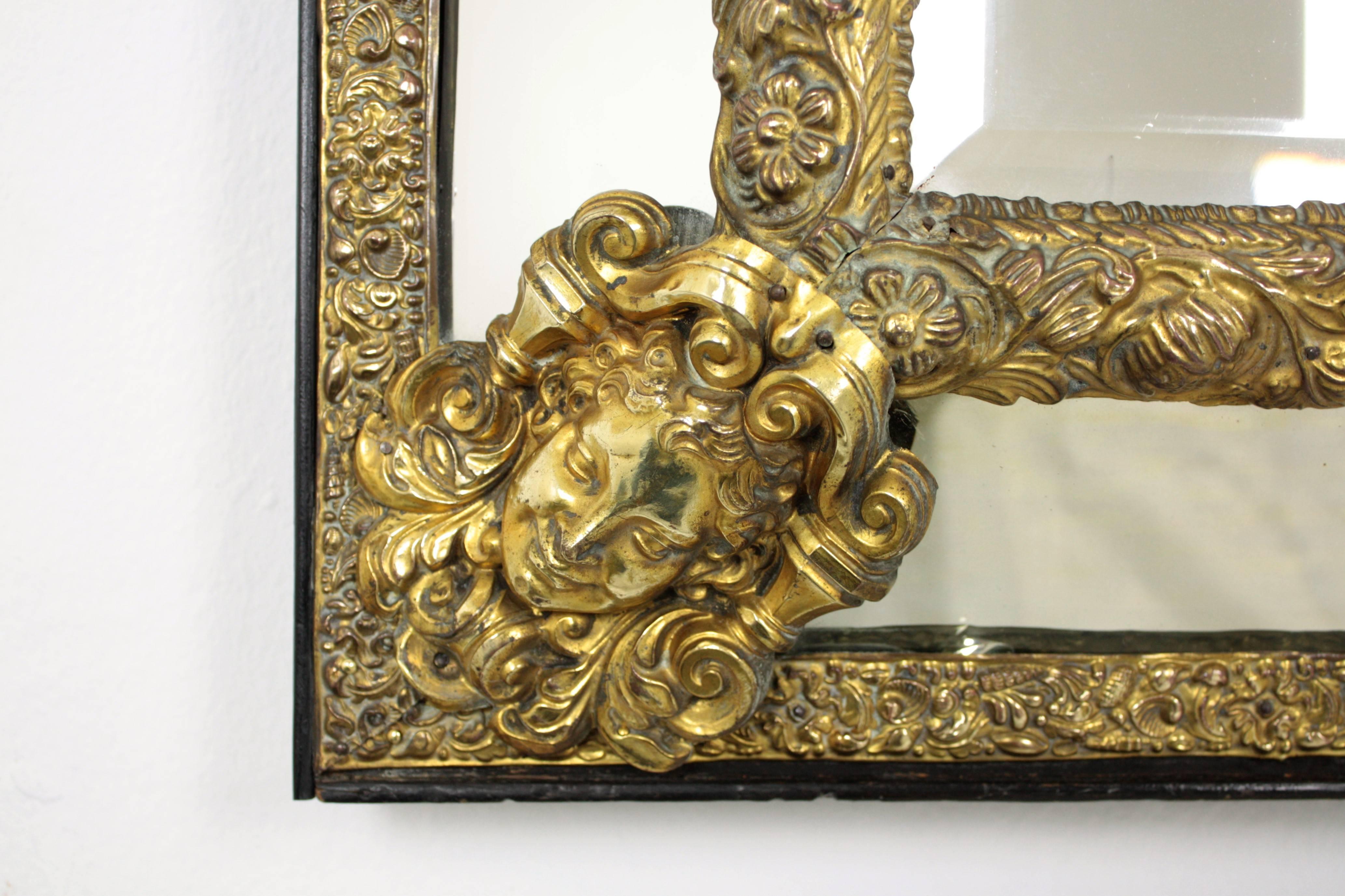 An elegant Napoleon III period mirror made with central beveled glass and four rectangular glasses joined between them by decorative brass repousse floral patterns, an elegant filigree repousse brass crest and scupltural faces adorning the