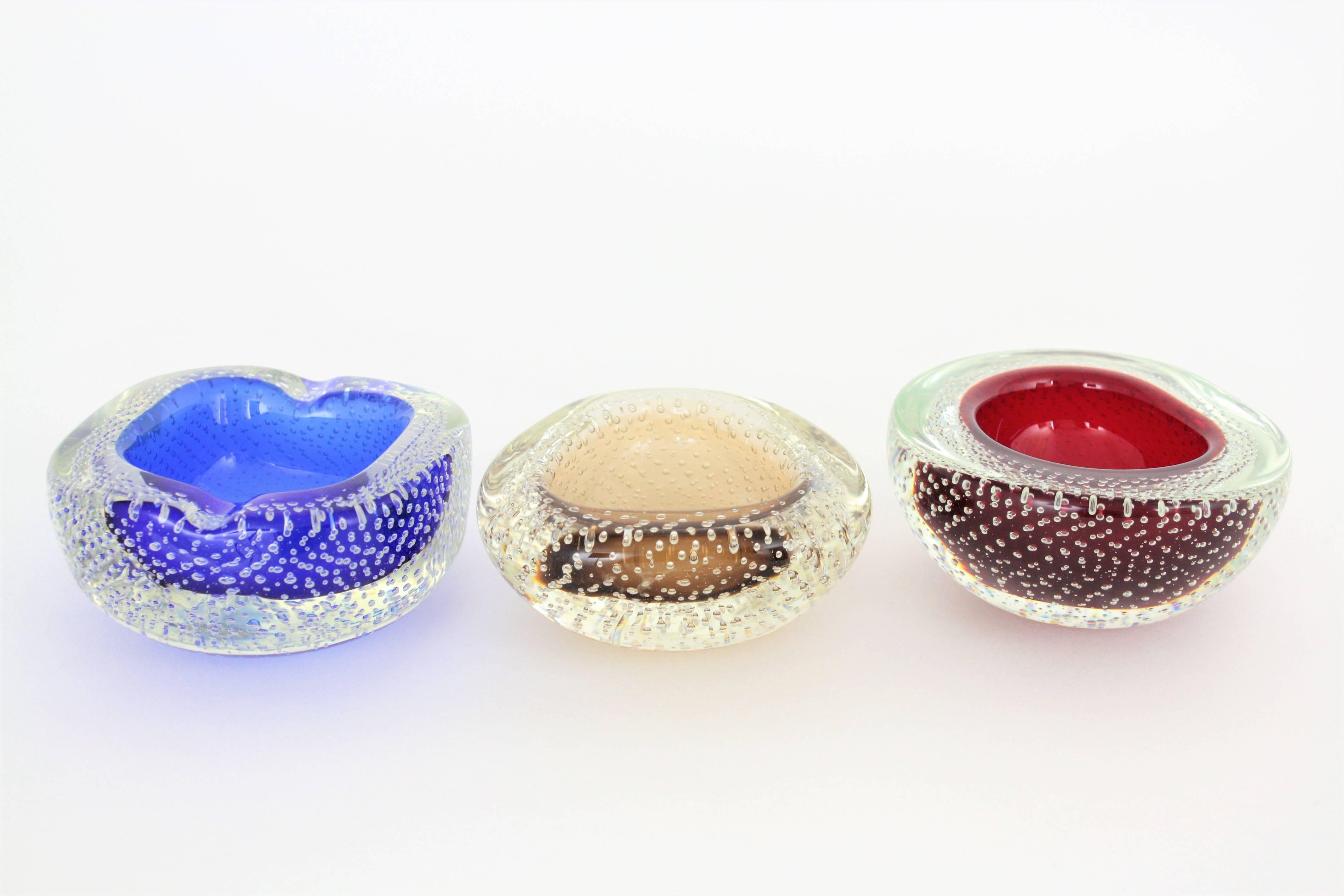 A beautiful set of three handblown geode Murano glass bowls attributed to Galliano Ferro. Red, blue and toffee glass cased into clear glass and a highly decorative controlled bubbles decoration. Each one has different shape.
The red and the toffee