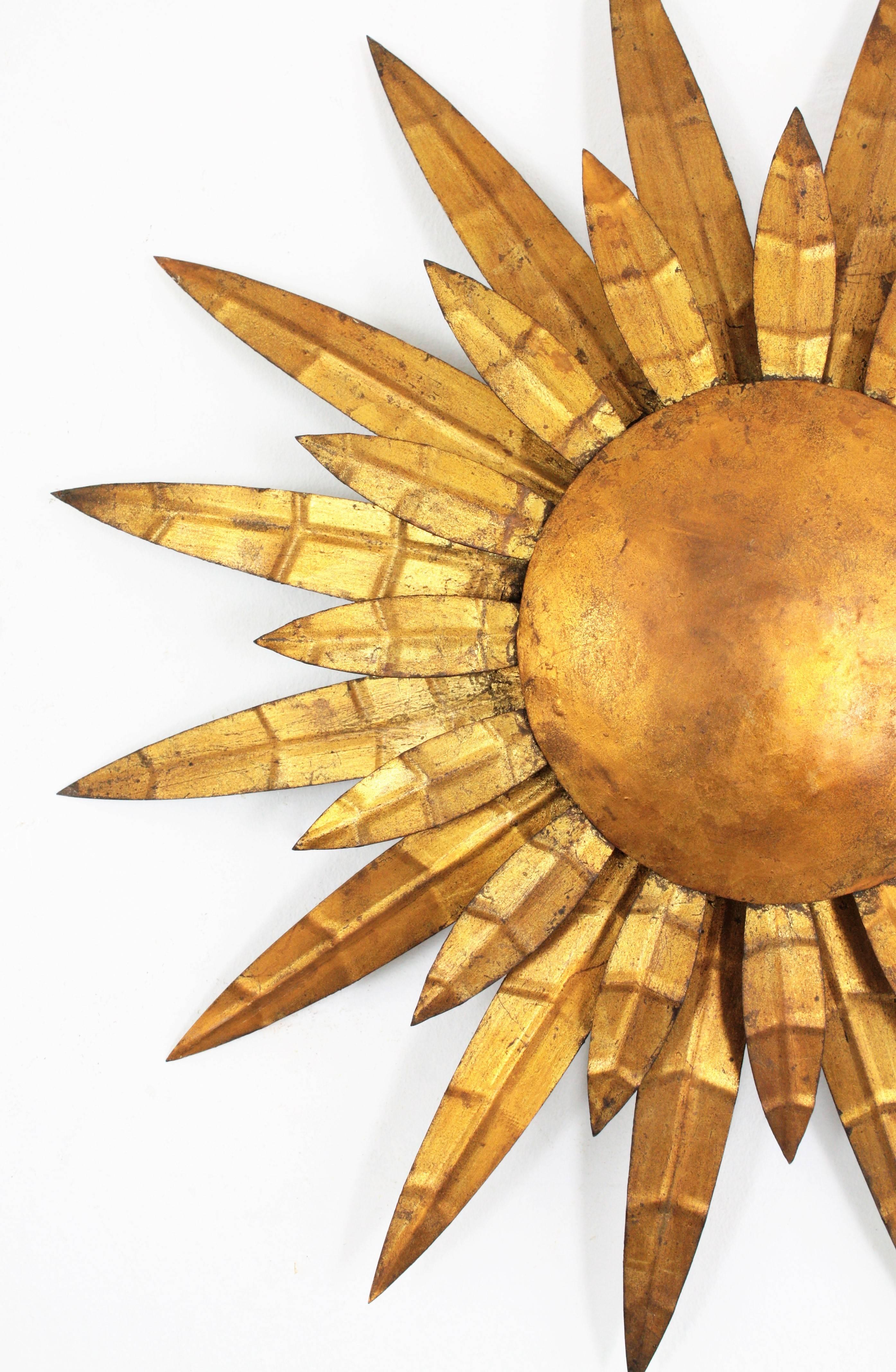 Beautiful two layered gilt iron sunburst wall decoration, wall sconce or ceiling light fixture. A hand-hammered piece with engraved details on its beams or leaves and gold leaf finish.
Its sunburst or sunflower shape is highly decorative.

France,