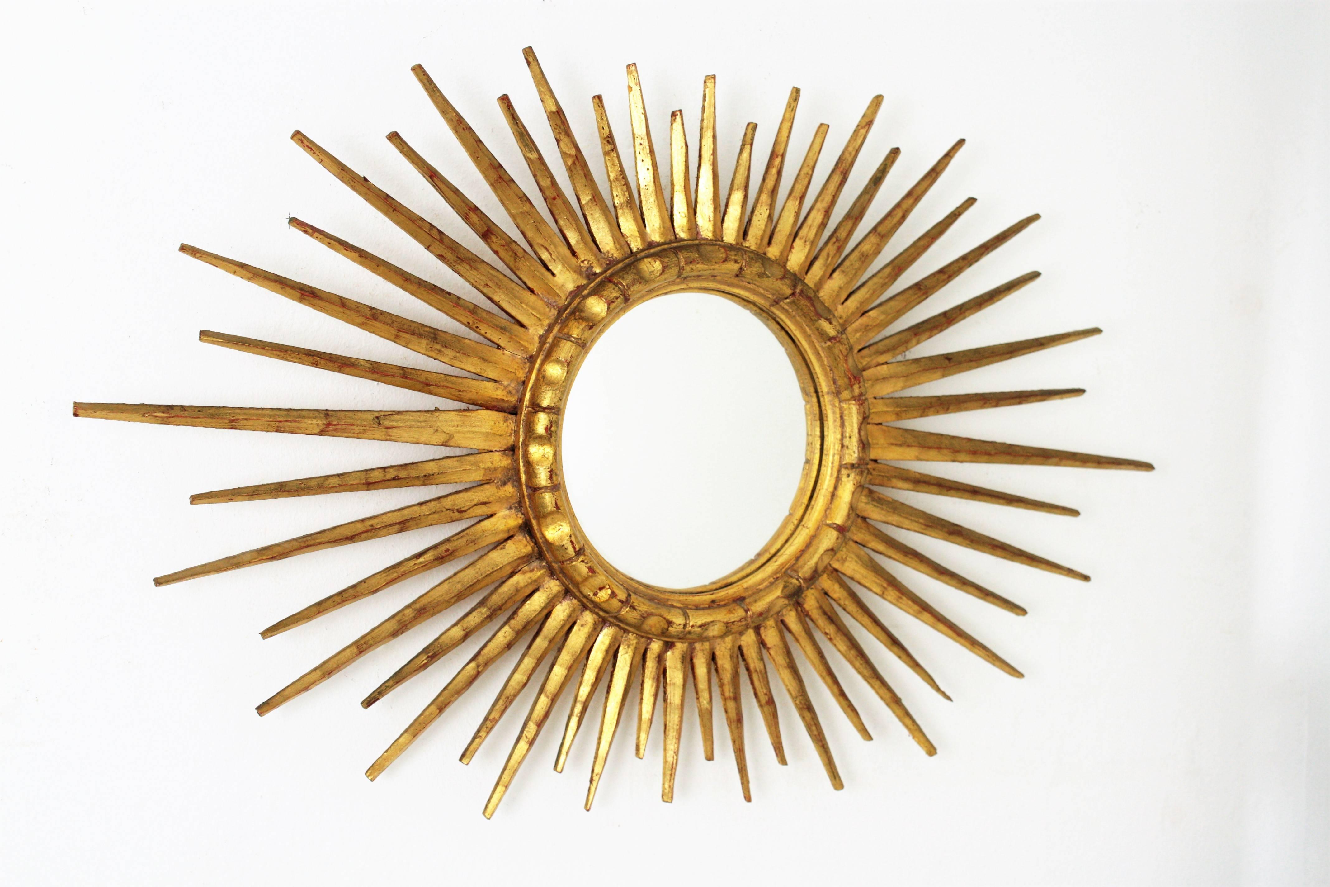 Amazing carved and giltwood Hollywood Regency oval shaped sunburst mirror with 24 karat gold leaf finish. This piece wears its original and excellent patina and due to its oval shape, with beams in different sizes it is highly decorative. It can be