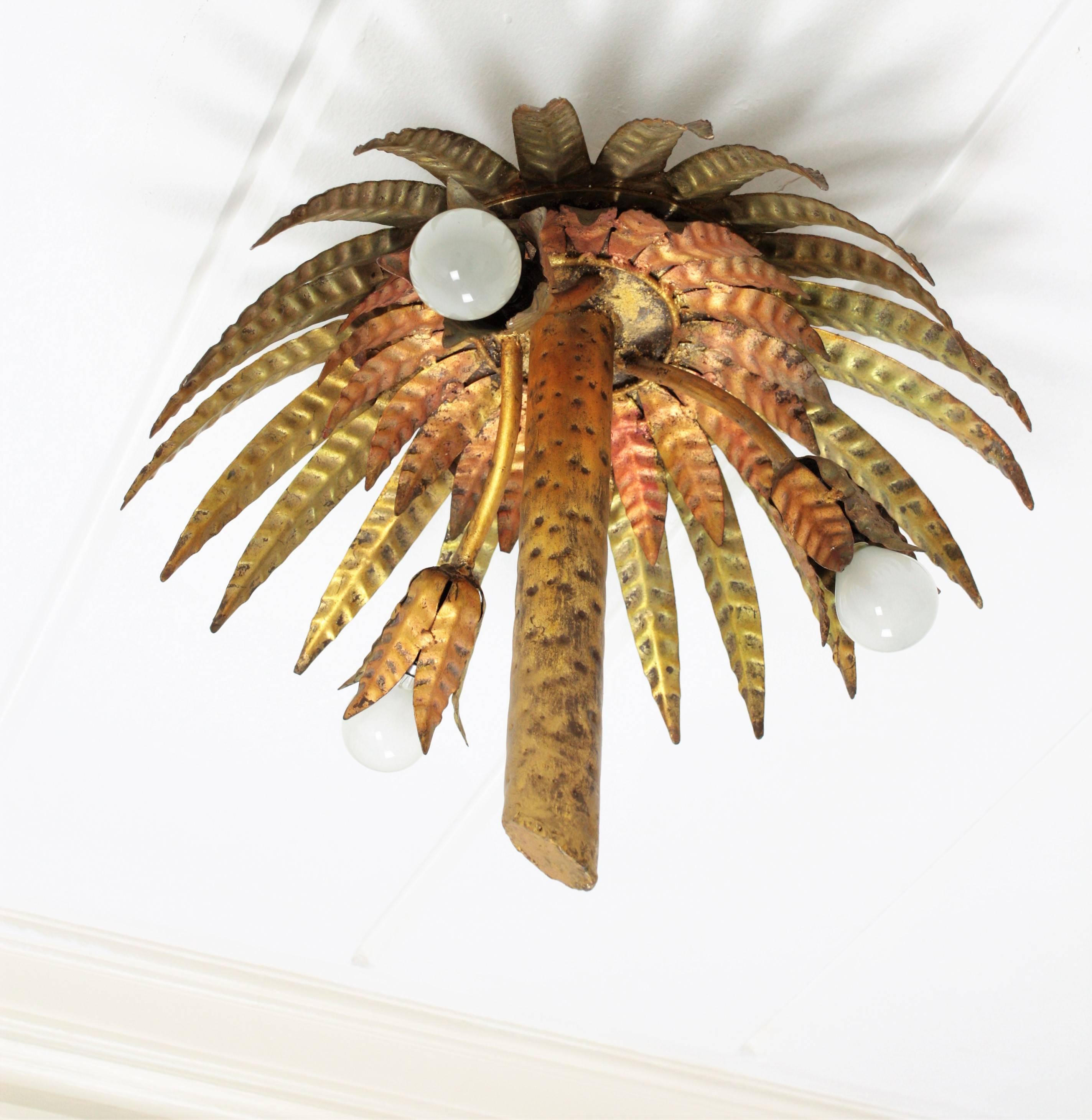 Unusual hand-hammered gilt iron palm tree ceiling light fixture. Spain, 1950s.
 This amazing piece has two layers of leaves and 3 branches finishing with flowers as bulb holders. This lamp wears its original vintage patina with gold leaf finish and
