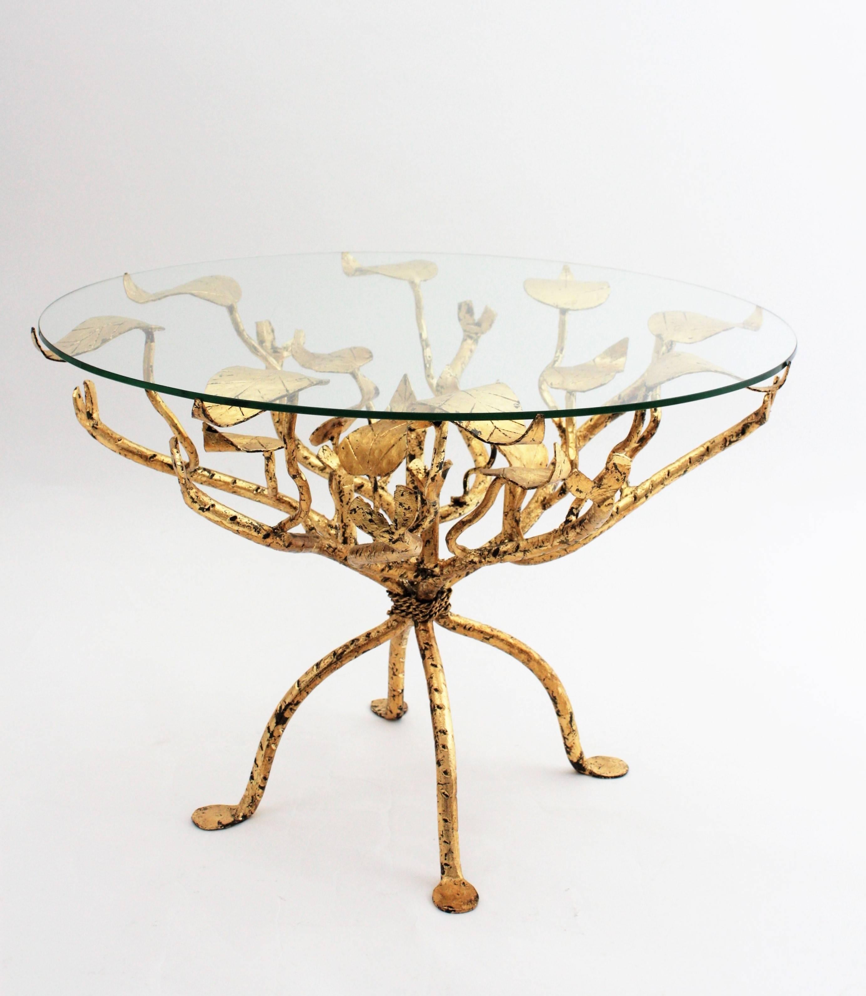 A luxury Hollywood Regency coffee table or side table with a hand-hammered naturalistic design of a tree or bush with branches and leaves holding a circular glass. 
France, 1950s.

Available more wrought iron and gilt iron pieces. Please kindly