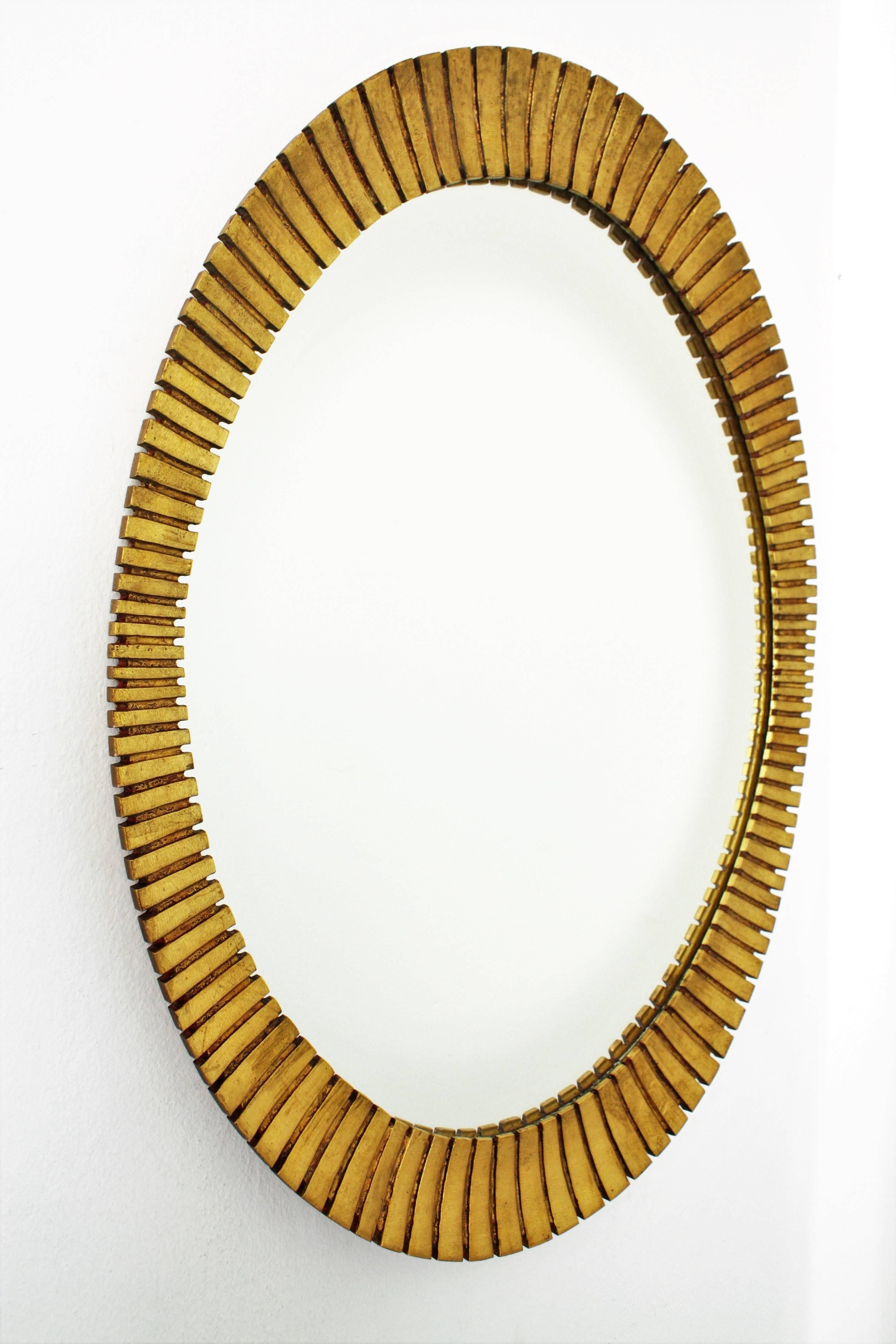 Gorgeous scalloped giltwood oval mirror with gold leaf finish in the Hollywood Regency style manufactured by the Spanish cabinet maker Francisco Hurtado. Ovoid shape frame with finely carved stripes and scalloped edge that make this mirror highly