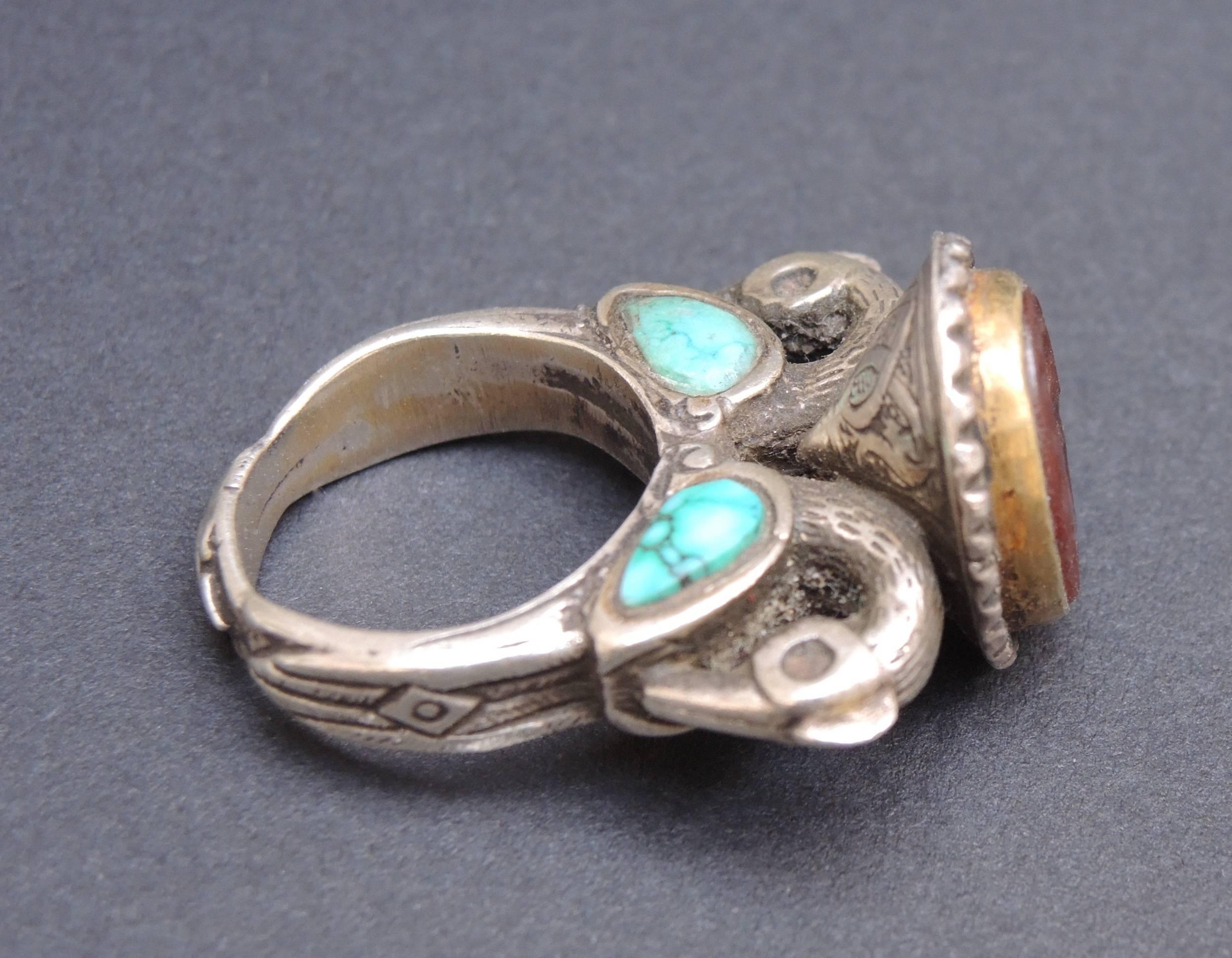 A stunning large ethnic tribal ring with carved carnelian stone intaglio. The ring is hand cast bronze plated in silver with a large bezel set intaglio carved carnelian stone flanked by stylised rams heads and turquoise stones.
The size is between