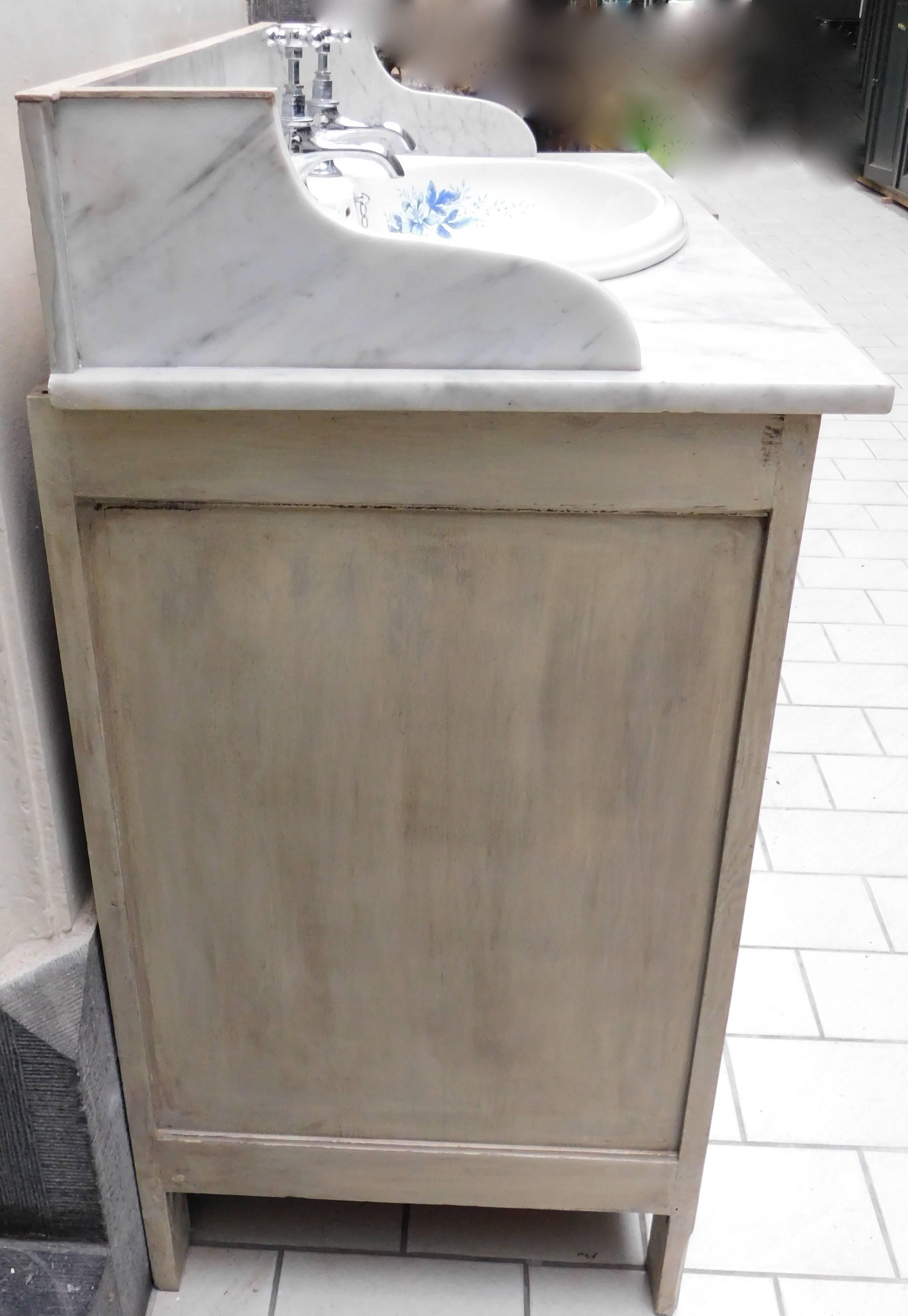 Circa 1910 English marble top oak sink vanity cabinet and mirror with patina painted finish.
Lovely victorian style blue and white porcelain sink with chrome faucets and stopper is set into the carrera marble top.
The bevelled glass mirror is shown