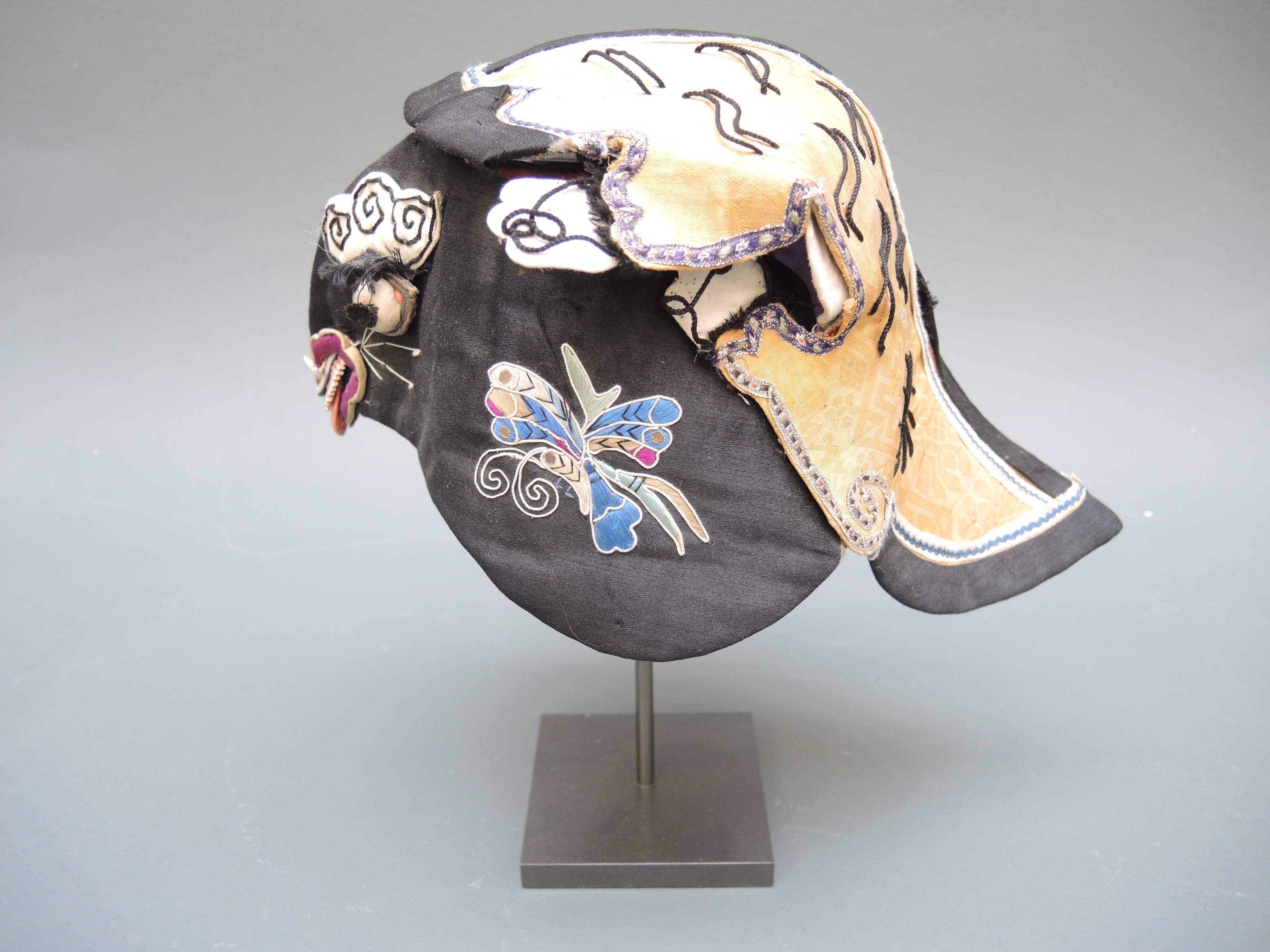 Chinese children's festival hats each with its own character. Fine silk hand embroidery of grasshoppers, flowers and butterflies adorn the two silk scholars hats while the other cotton hat is made in the shape of a noble tigers head celebrating the