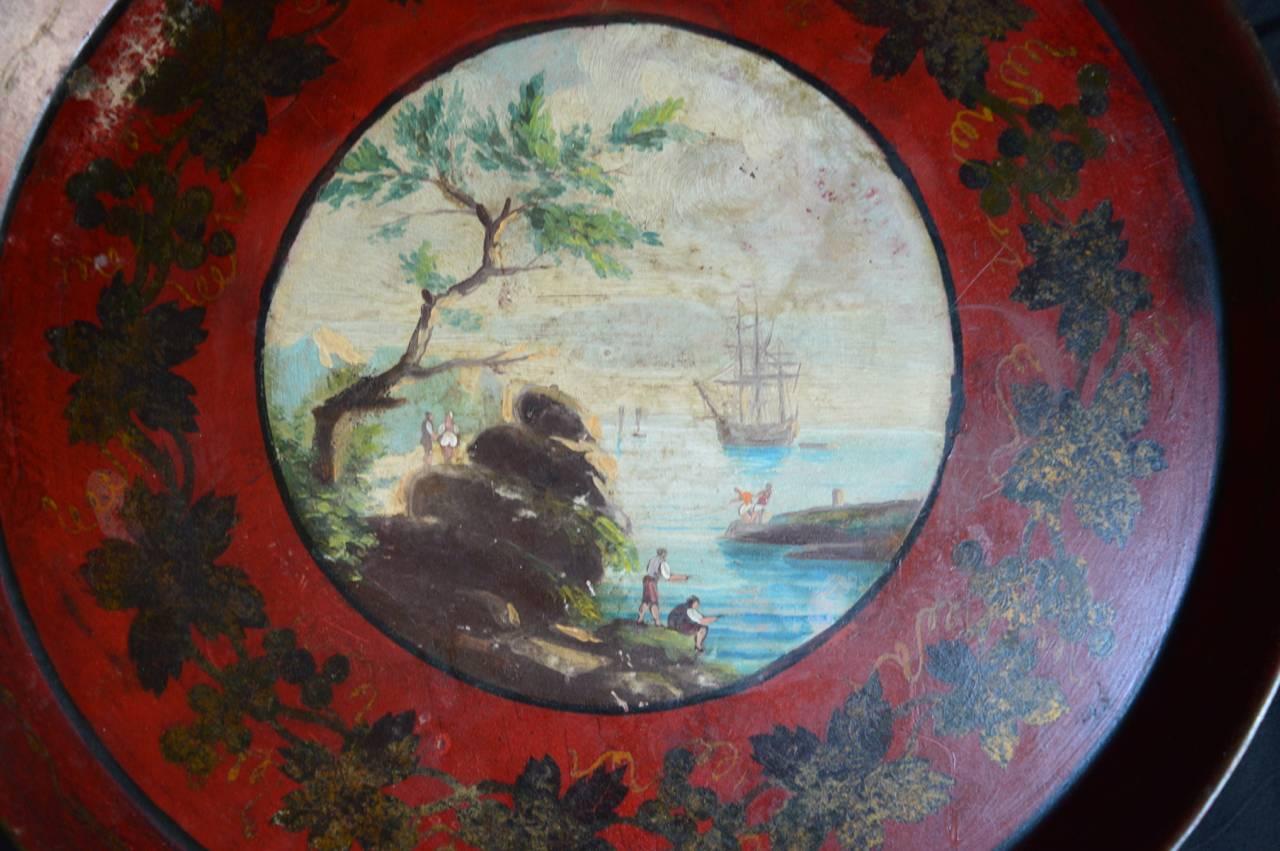 Early 19th century French tole tray in remarkably good condition. The tray itself is a deep red with delicately painted gold leaf border and a charming central painting depicting a seaside harbor scene.
Great bar tray, or make a base for it to use