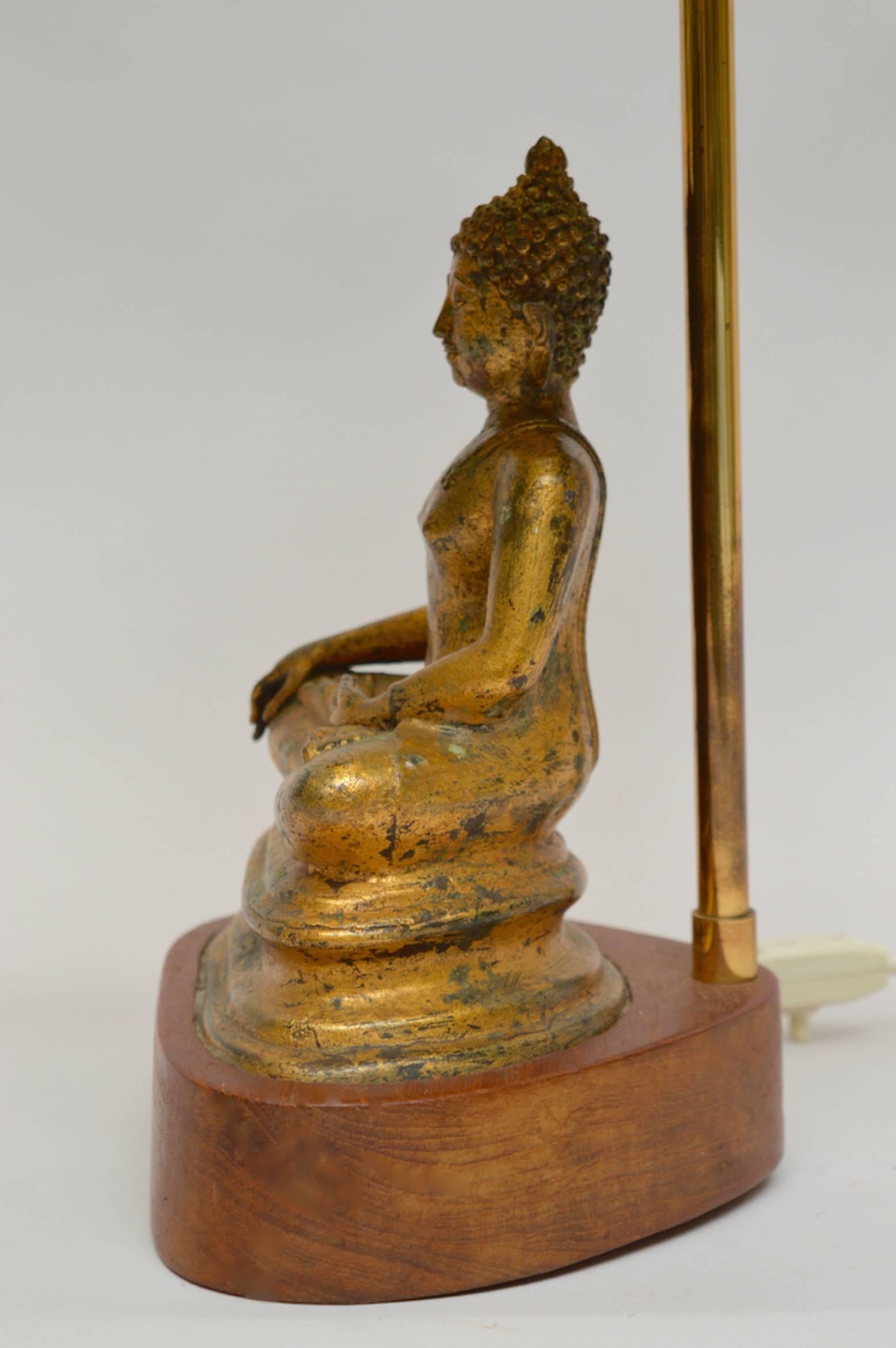 Original gilt bronze Buddha lamp from the 1940s. The meditating Buddha is mounted on a solid teak wood base hand-carved especially to fit this Buddha.
The silk pagoda style shade is original to the lamp and adds the perfect finish.
The high