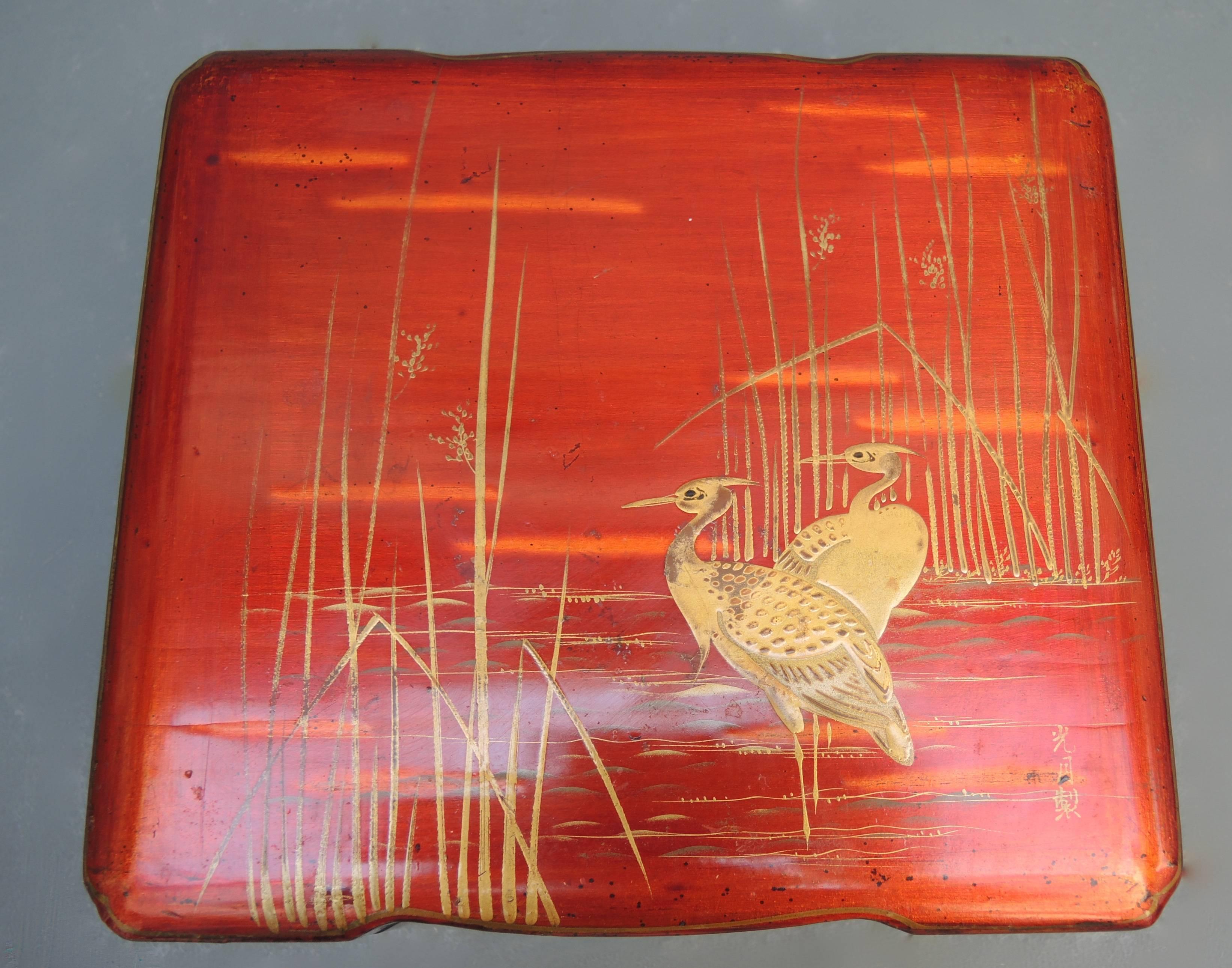 Japanese lacquered wood box in a rich burnt orange color with a scene of cranes in the marsh painted in gold and signed lower right, circa 1920.