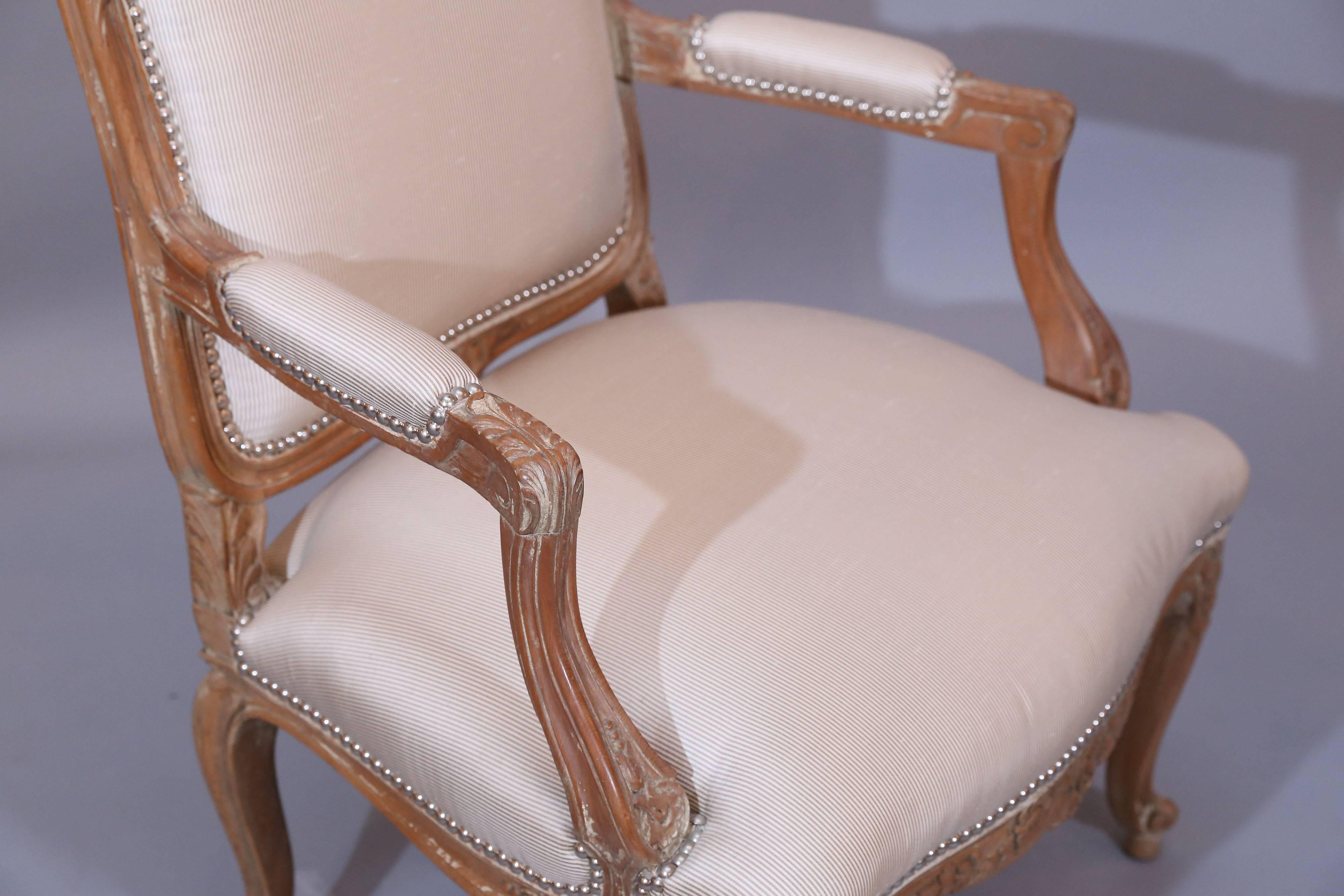 Very handsome reproduction fauteuils with gracefully curved shaping. Chairs have floral carvings on top of back and the apron. Acanthus leaves are
carved on knees.

Upholstery is a taupe and cream thin stripe silk finished in
nailhead trim.