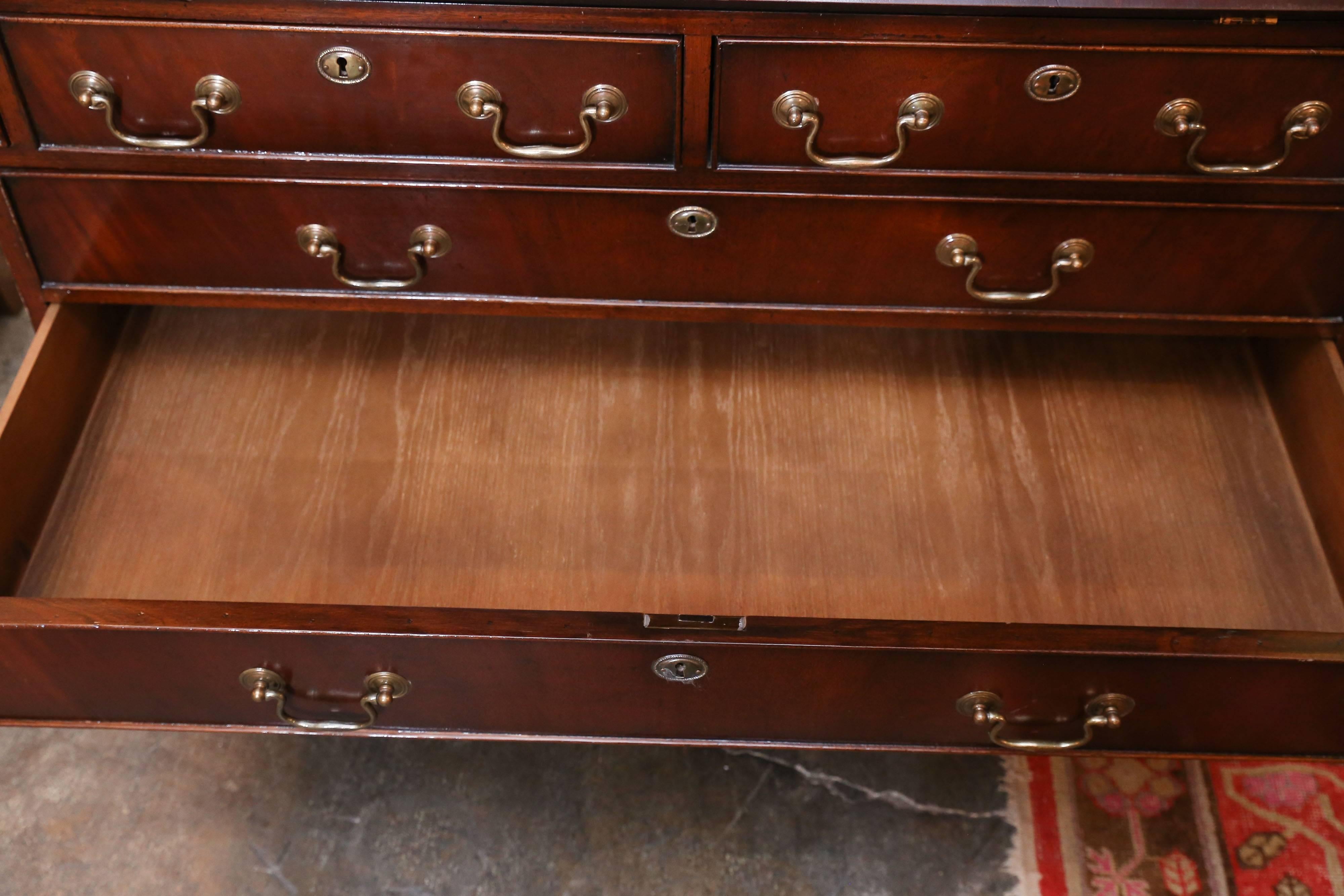 English mahogany secretary with very handsome desk details under slant top.

Upper cabinet includes three mahogany shelves, a dentil molding top
and crowned glass.

Base features three small and three long drawers.

Designed and imported by