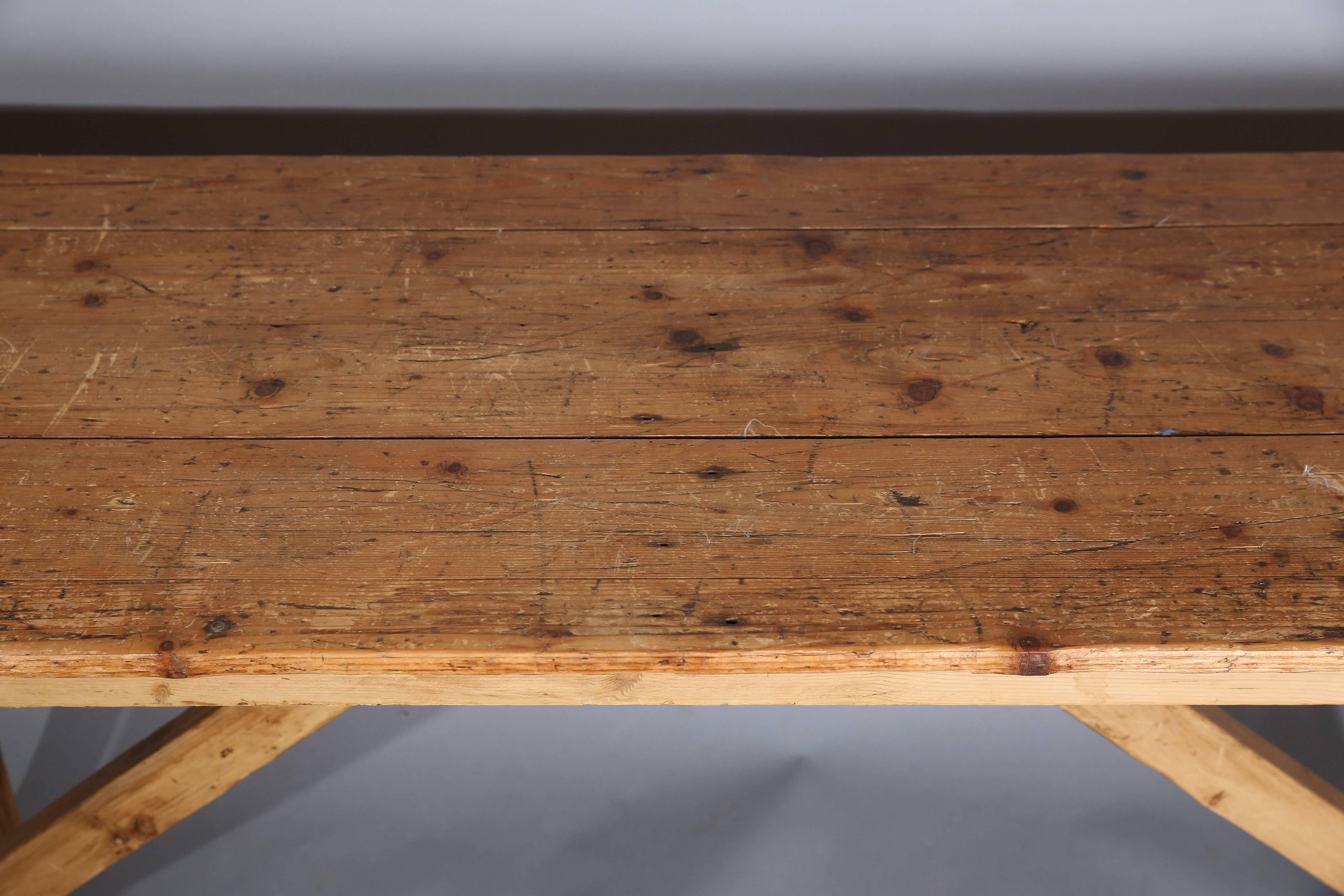 Very simple console or worktable has plank top, straight legs, simple apron and trestle stretchers.

Very rustic.

