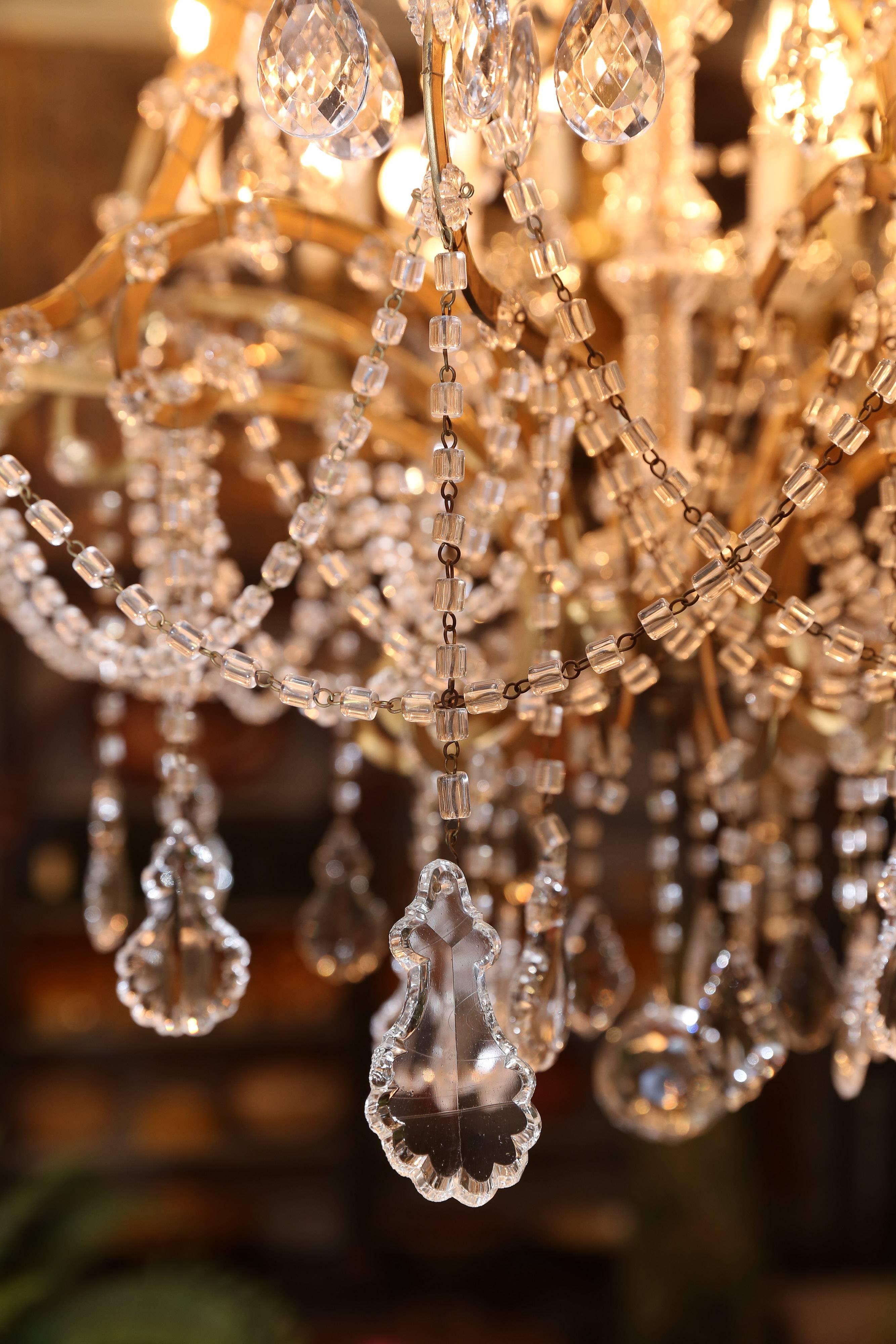 Beautiful two-tiered Italian chandelier has 18 arms, a brass cage and lots of crystal swags draping entire piece.

Each swag has a larger crystal suspended from each arm.

18 glass Bobeche have a row of beads with larger crystal, as