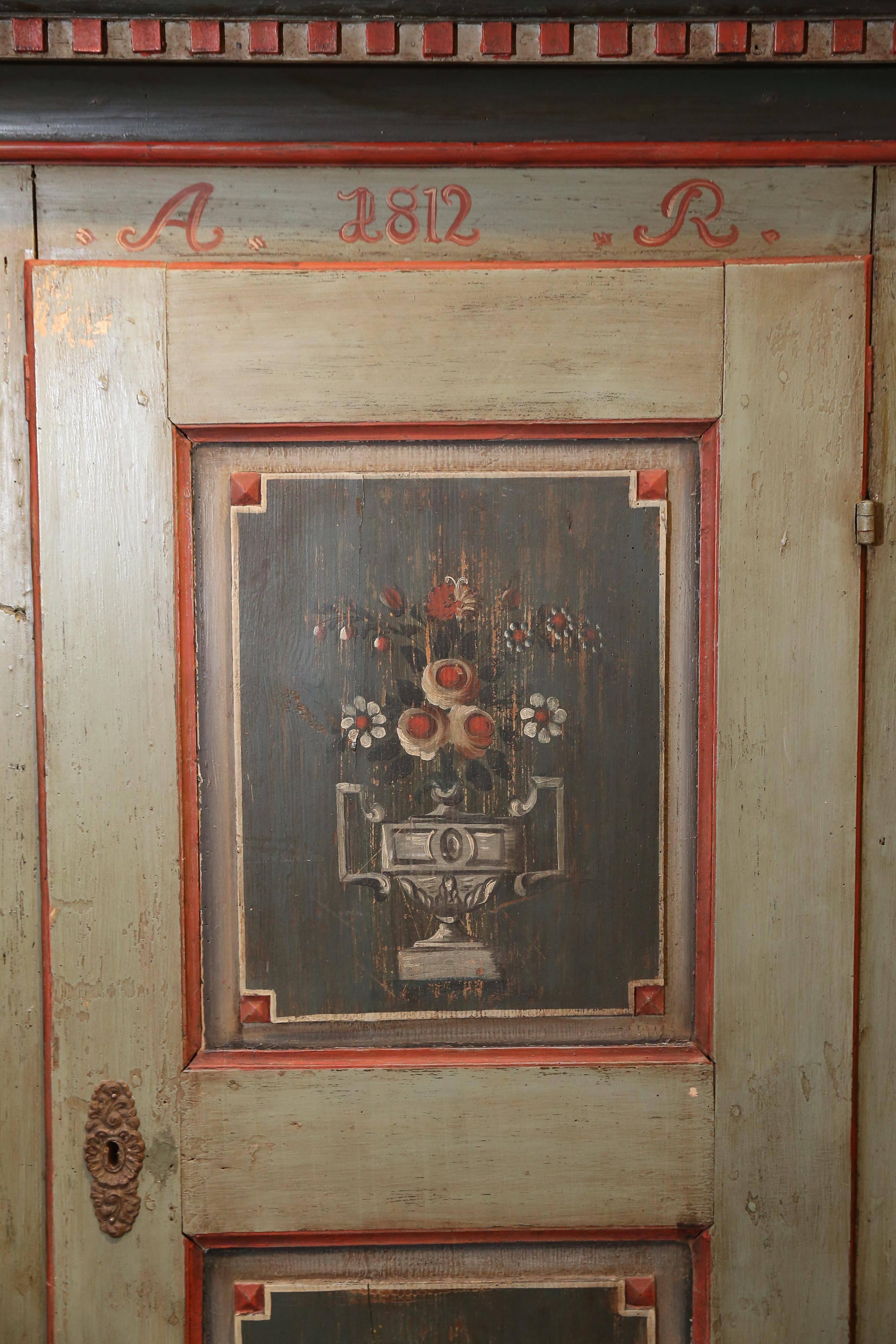 Single door Austrian cabinet has a blue background and decorated with painted panels.

Front of cabinet features two panels with painted urns containing flowers, on a black
background outlined with a red band.
Side panels are plain black with