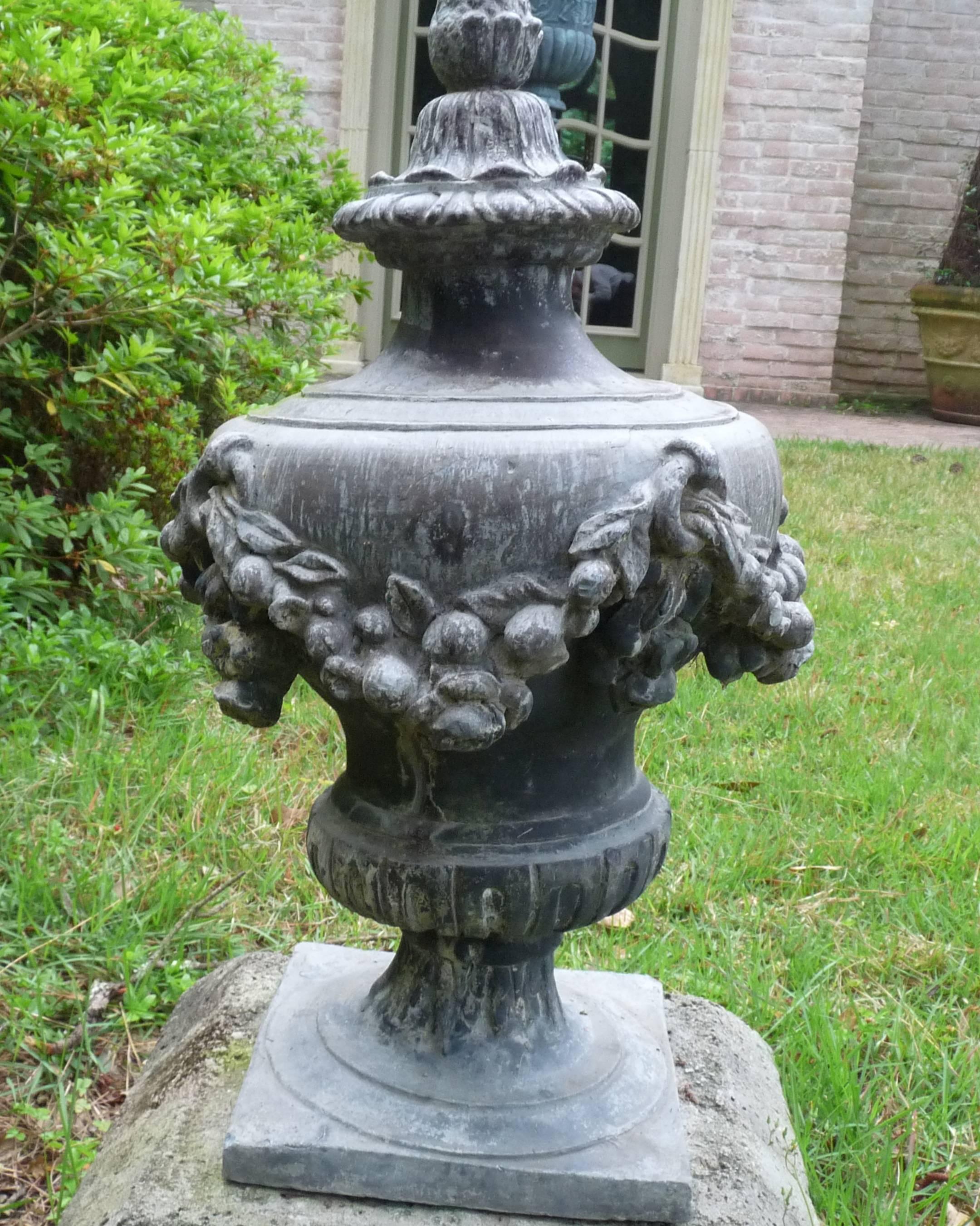 Handsome Georgian lead lidded urns with swagged garland design, fluting, and a pine cone design on top.

Urns sit upon a square base

   