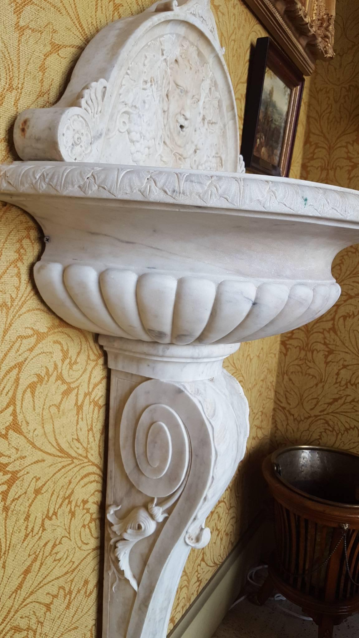 White marble wall fountain features the face of Bacchus surrounded by grape clusters and grape leaves.

Bowl of fountain bowl is fluted and rests on a single pedestal with more patterns in relief.