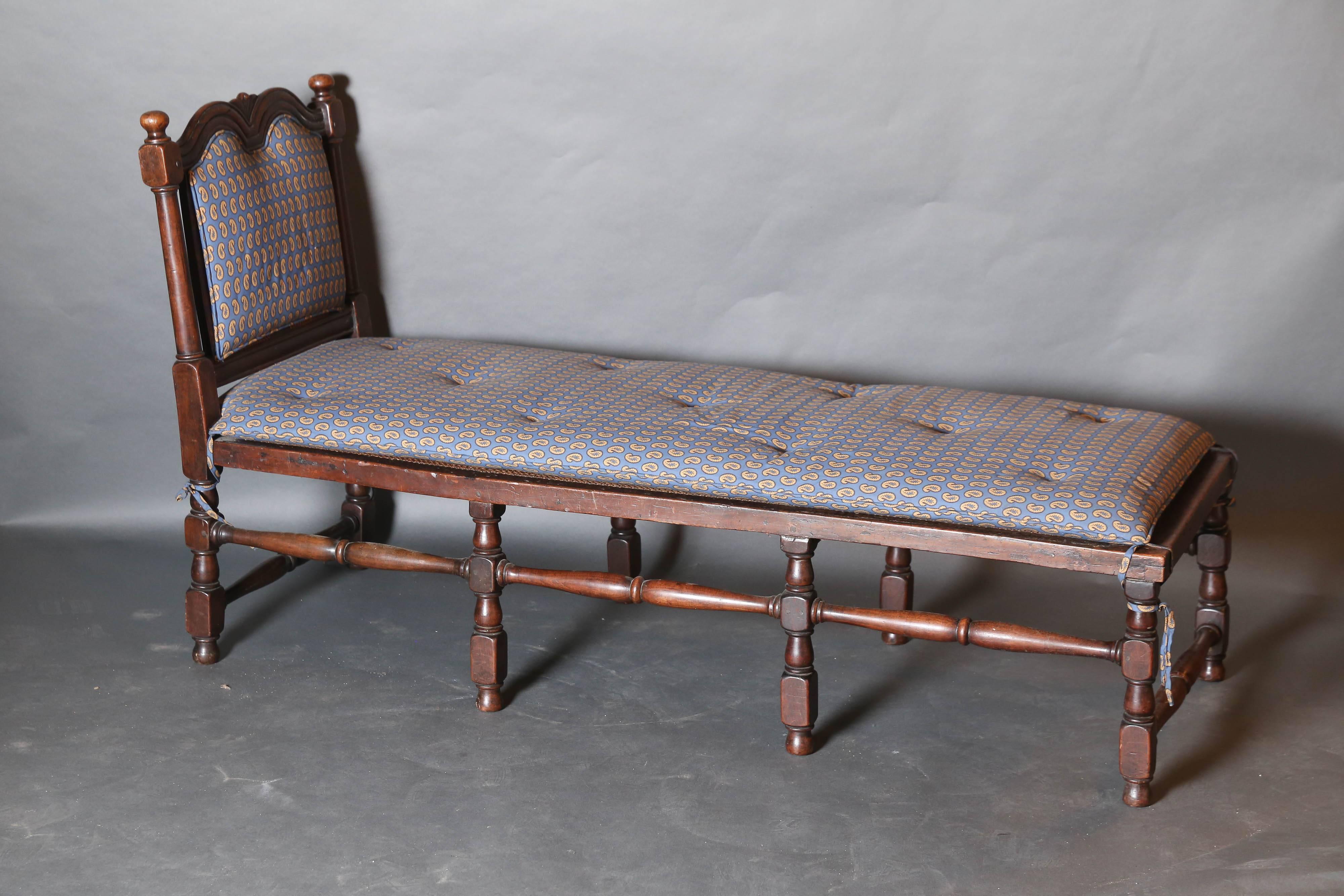 Charles II carved walnut chaise with cane seat an upholstered back, plus loose cushion. A Royal Crown is featured on headboard with a pair of finials.

Legs and stretcher are all turned.