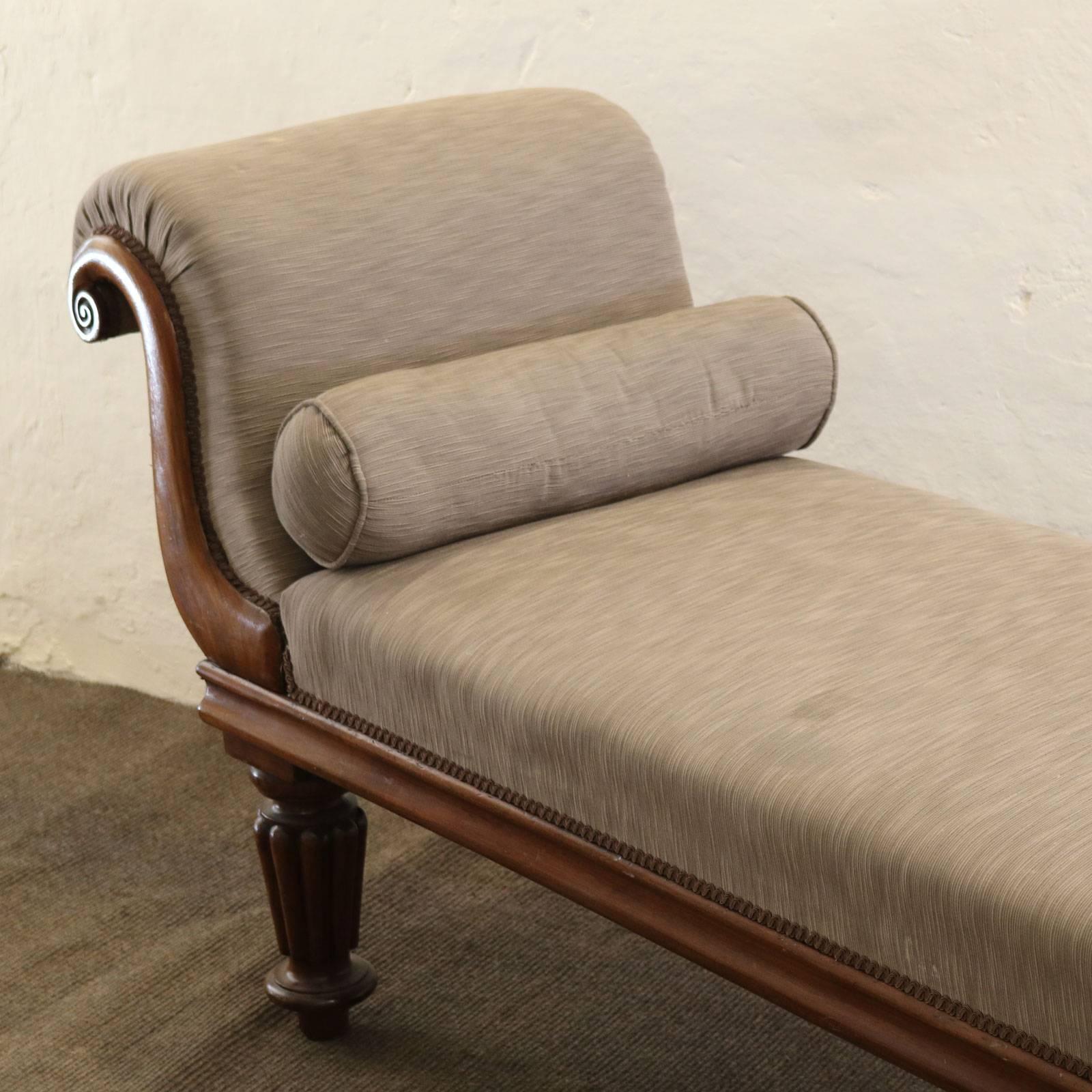 A Victorian mahogany chaise longue with roule end and carved feet. The grey chenille upholstery is a later addition and is showing some marks.