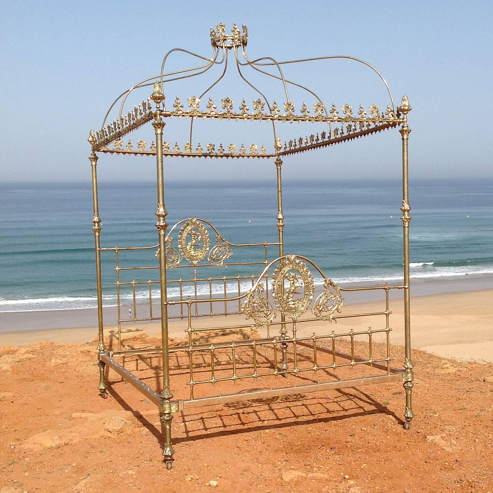 A magnificent all brass four poster bed with tall posts, decorative brass fittings and central brass plaques depicting cherubs amongst vines and foliage. The etched posts and decorative brass fittings on the posts and at the "kneecaps" and