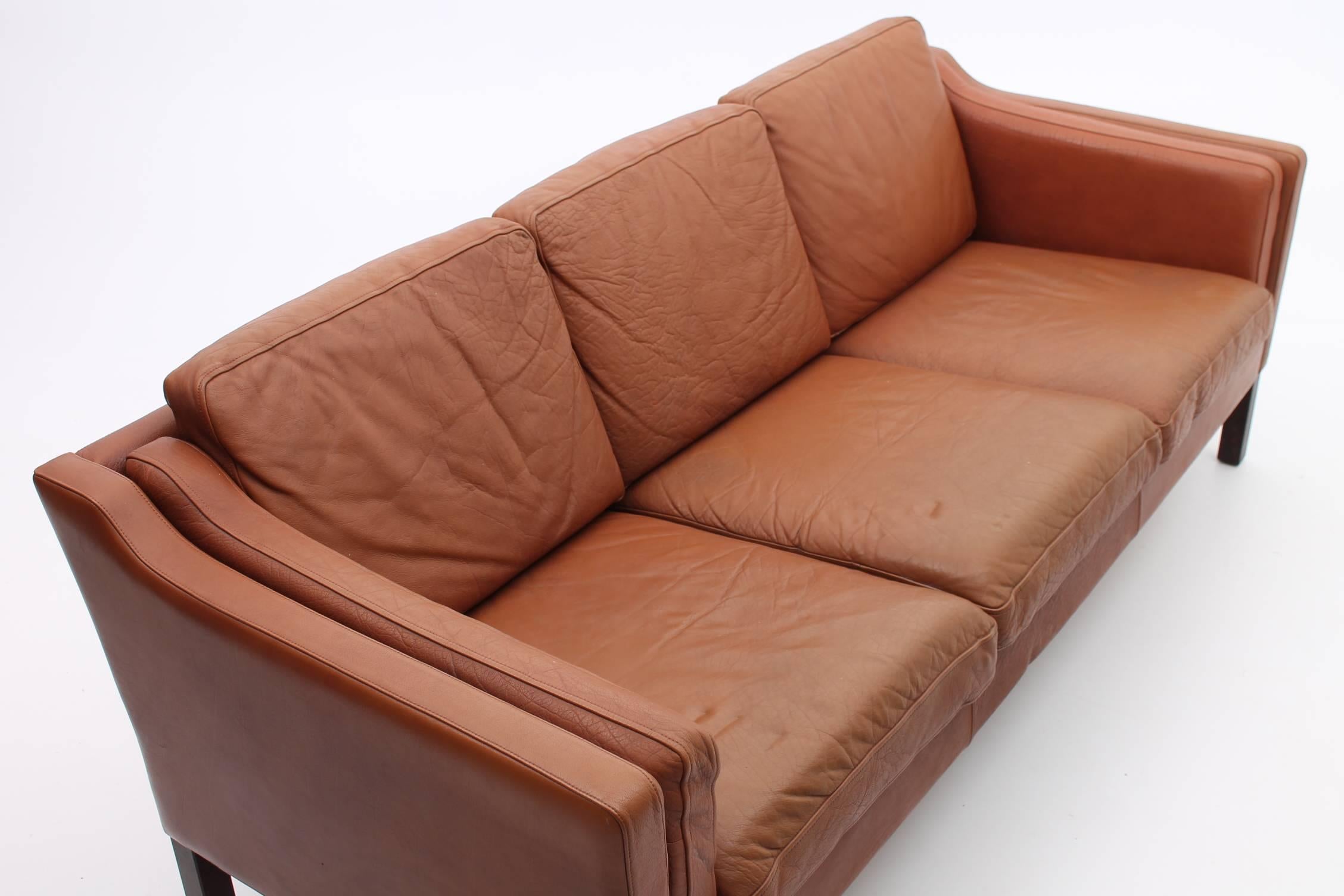 Beautiful chestnut colored leather sofa. This sofa is in excellent condition, with its original leather in tact. There are four wooden legs that give the leather a warm yet Minimalist feel.