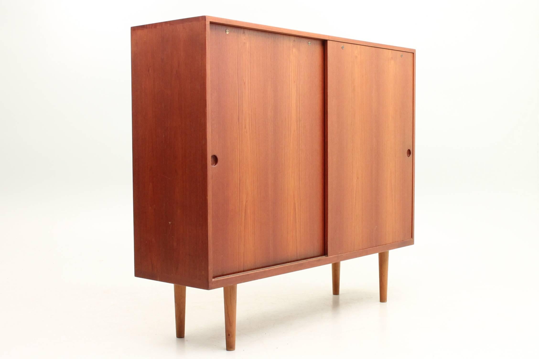 Teak RY26 cabinet designed by Hans J Wegner for Ry Møbler, circa 1959. This cabinet or highboard is a rare find and is in excellent vintage condition. This piece features fully adjustable shelves and two slim drawers. The sliding doors pull from a