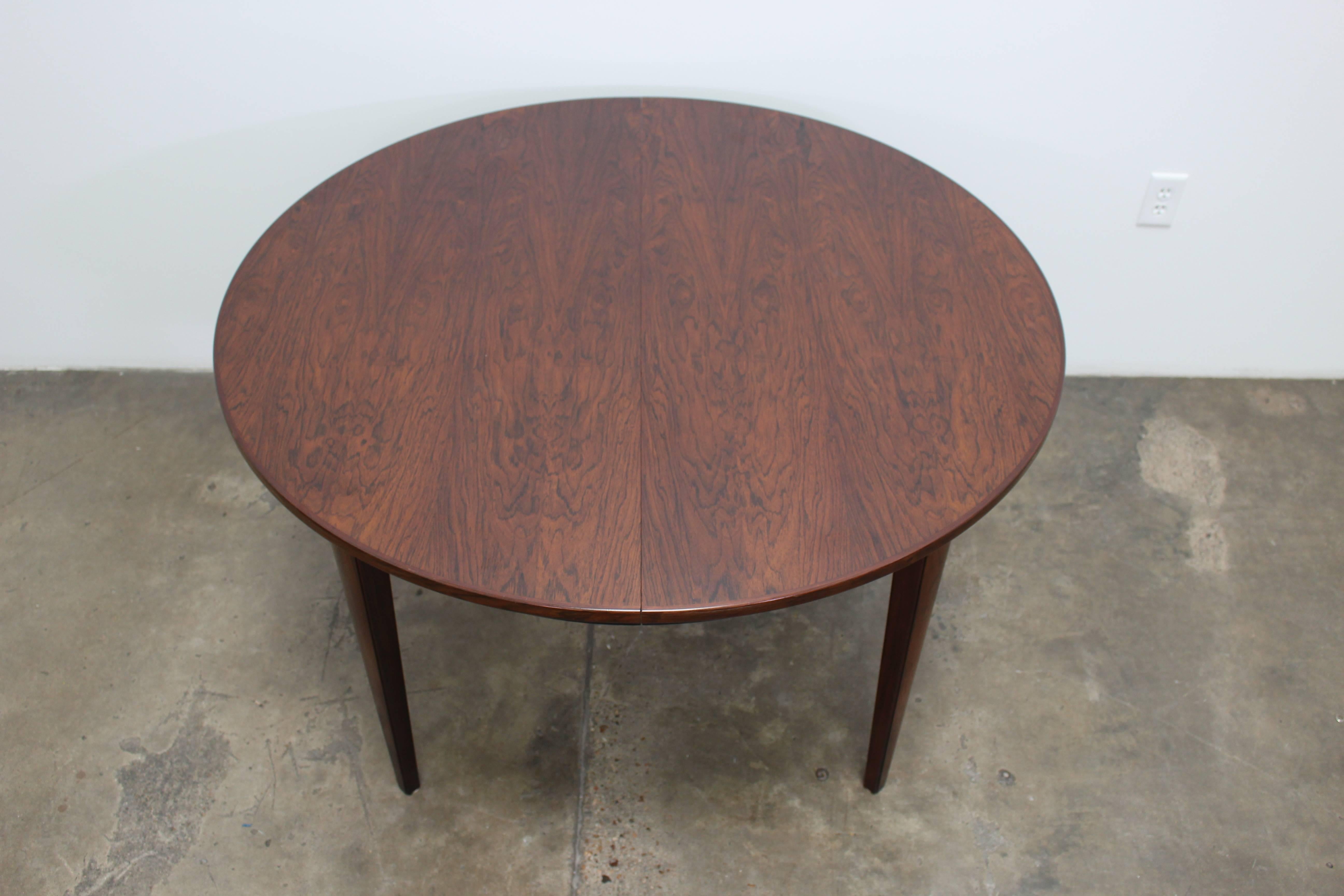 Circular rosewood dining table designed by Gunni Omann for Omann Jun. The rosewood on this table has a beautiful, intense grain and a shiny finish. There is a thin black band at the bottom of the apron that encompasses the entire table.
