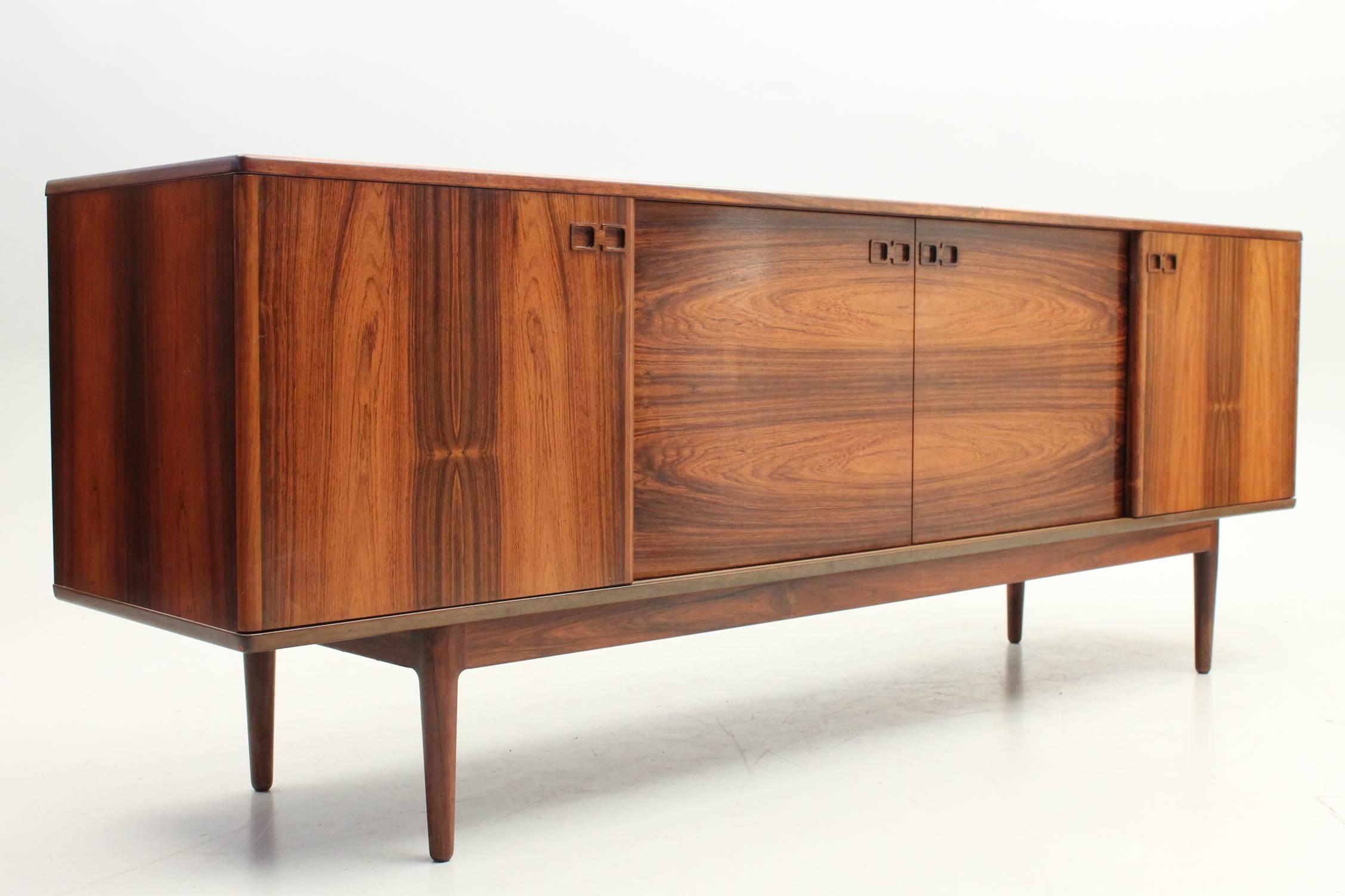 Long credenza designed by Ib Kofod-Larsen for Faarup Møbelfabrik in the 1970s. This gorgeous credenza features four sliding doors, the compartments on either end features an adjustable shelf while the middle has drawers. The rosewood has a beautiful