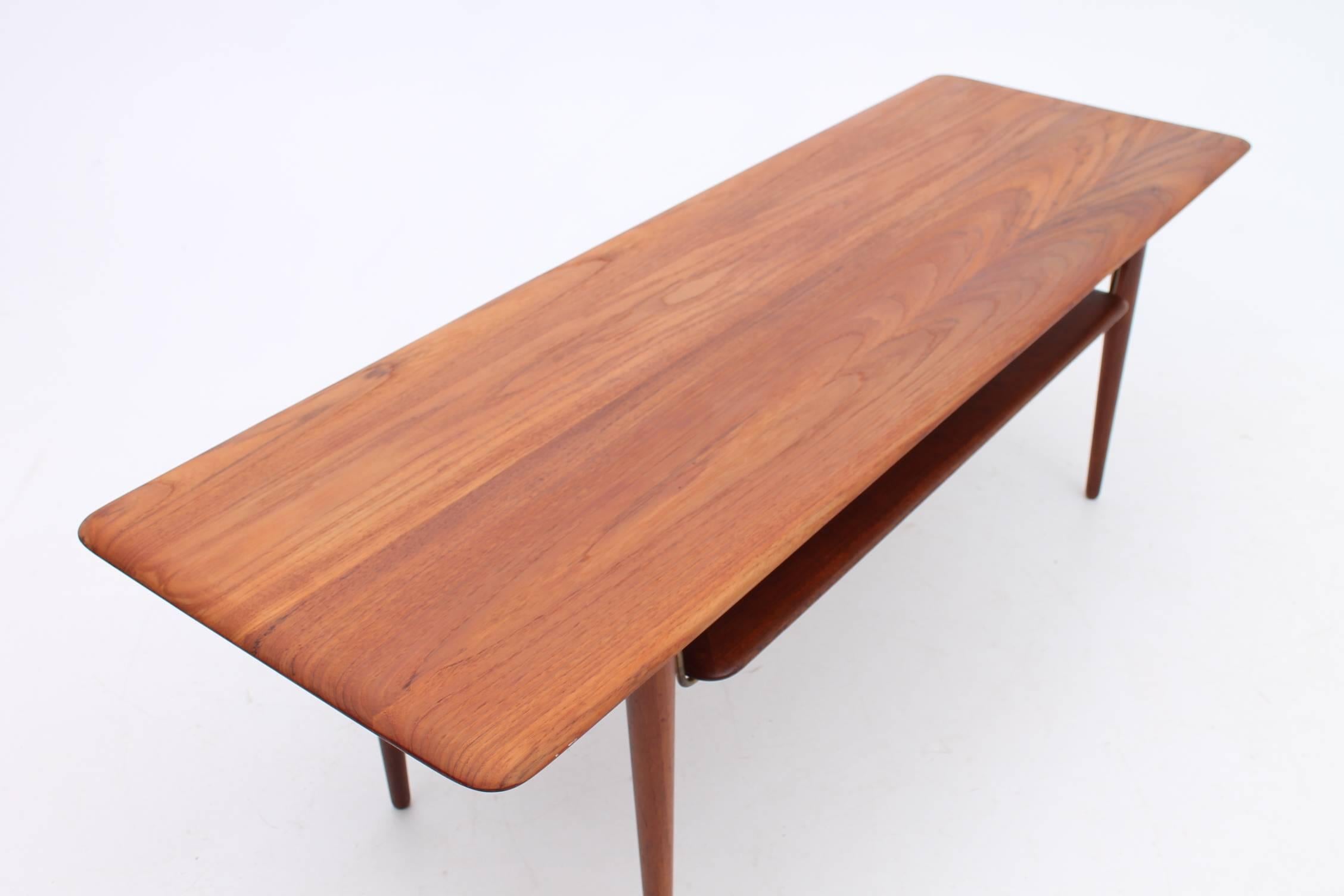Beautiful teak coffee table designed by Hvidt and Mølgaard for France & Daverkosen This gorgeous table has a floating rack underneath the tabletop for extra storage that is attached with brass fasteners. This table has been professionally
