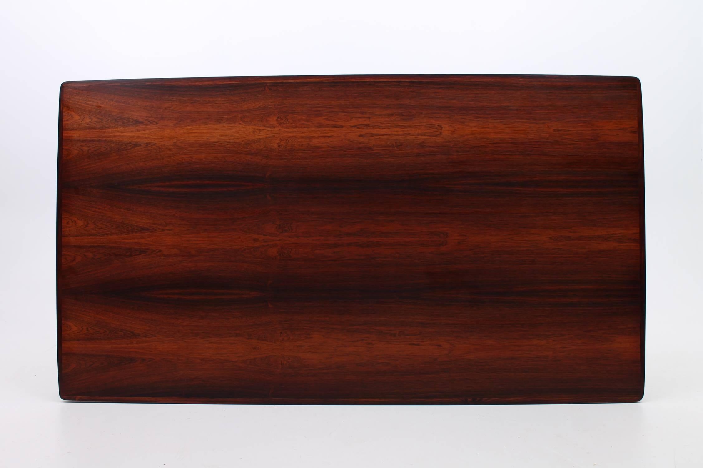 Stunning rosewood designed by Arne Vodder for Sibast Furniture. This huge table has two self storing leaves that discreetly hide underneath the tabletop. The vibrant rosewood grain adds a level of elegance to the minimalistic table. The table has