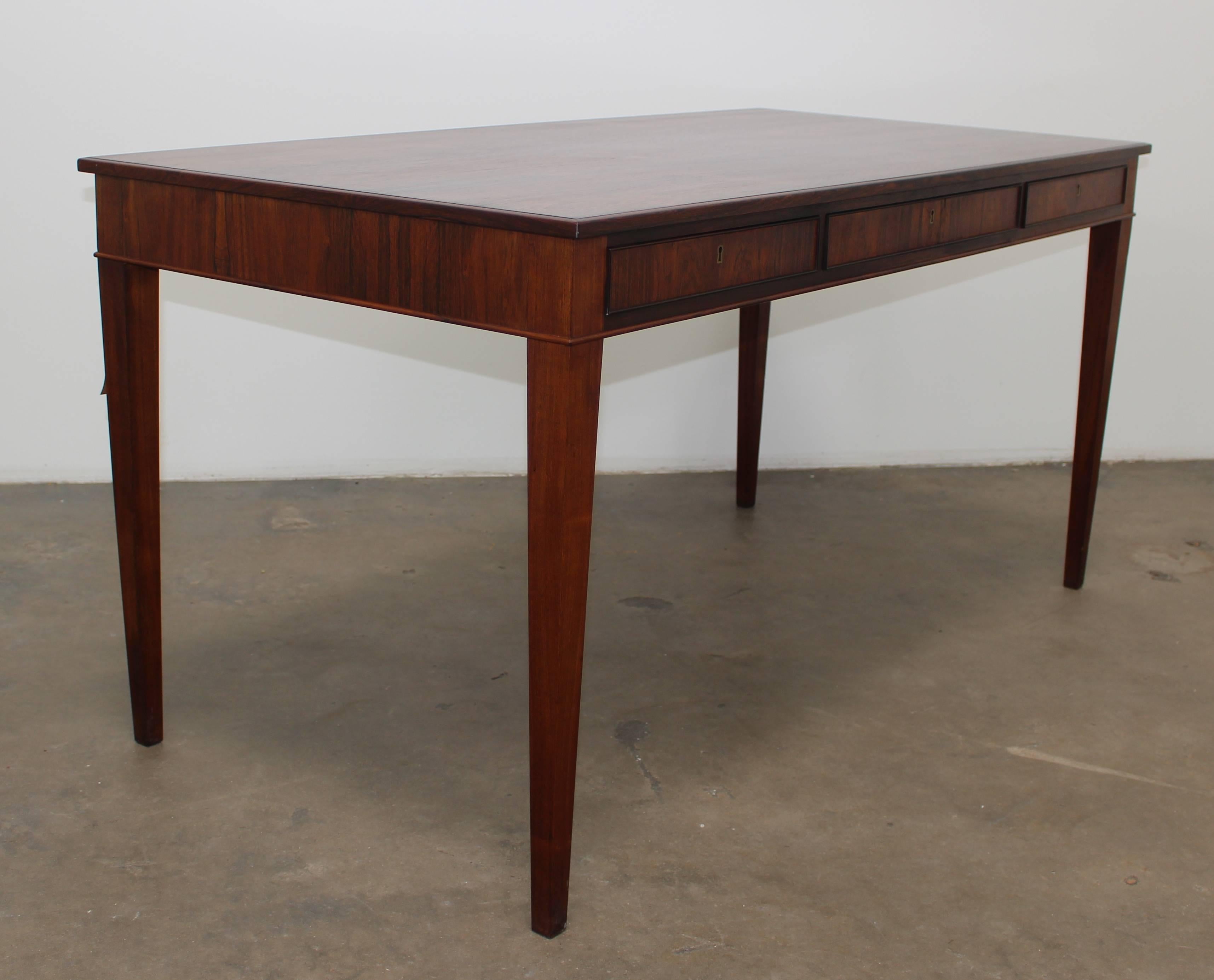 Beautiful dark rosewood desk that is modeled in the style of Frits Henningsen. This beautiful writing table is a minimalist design with three drawers that are inconspicuously hidden near the tabletop. All of the drawers have the original key and