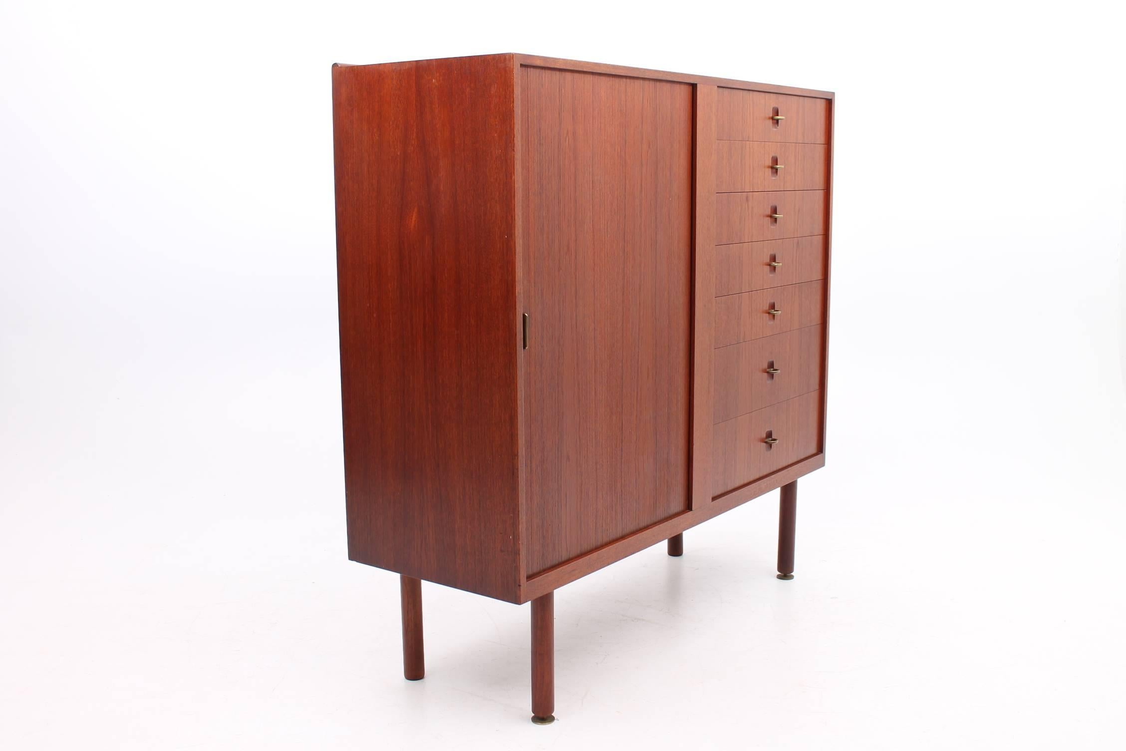 Beautiful cabinet made of teak by Aksel Bender Madsen for Ejnar Larsen. The details on this cabinet truly set it apart from the rest. The left half of the cabinet features a roll front tambour door with a brass handle and two adjustable shelves on