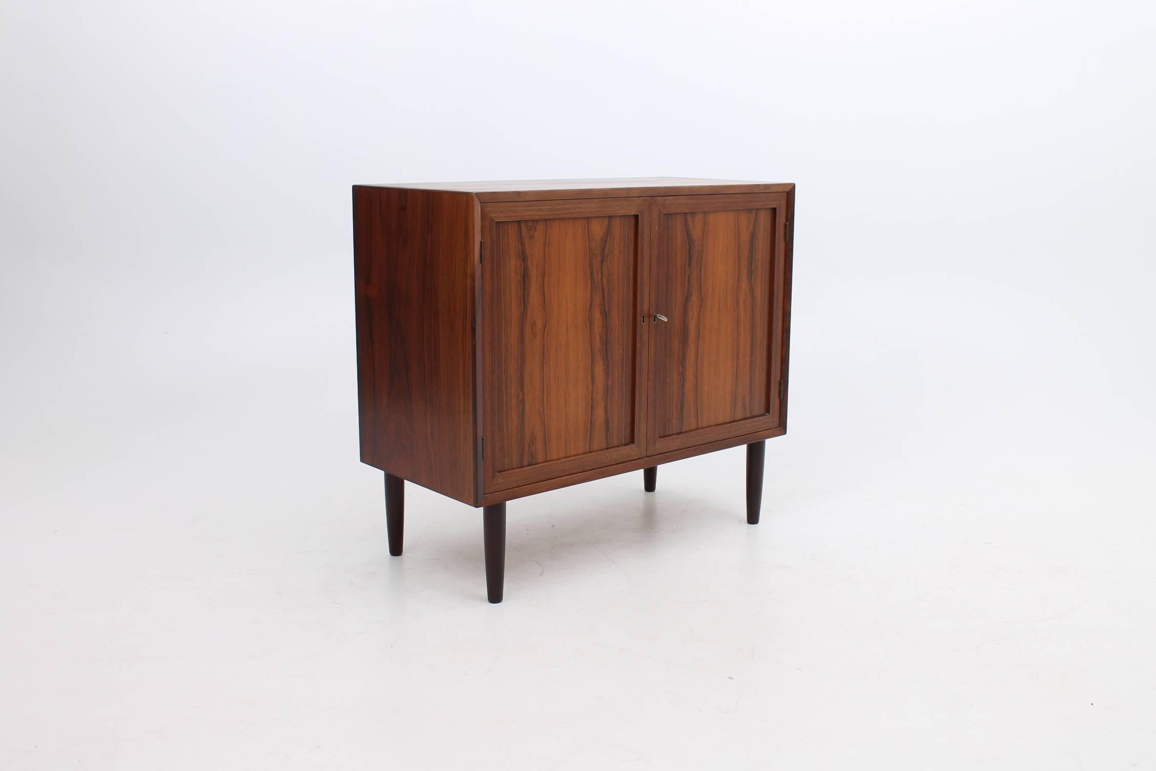 Small size cabinet designed by Lyby Møbler made of rosewood. This cabinet has a lock and key to open either one of the doors. The shelf inside is adjustable to accommodate many different items of different sizes and heights. This cabinet would work