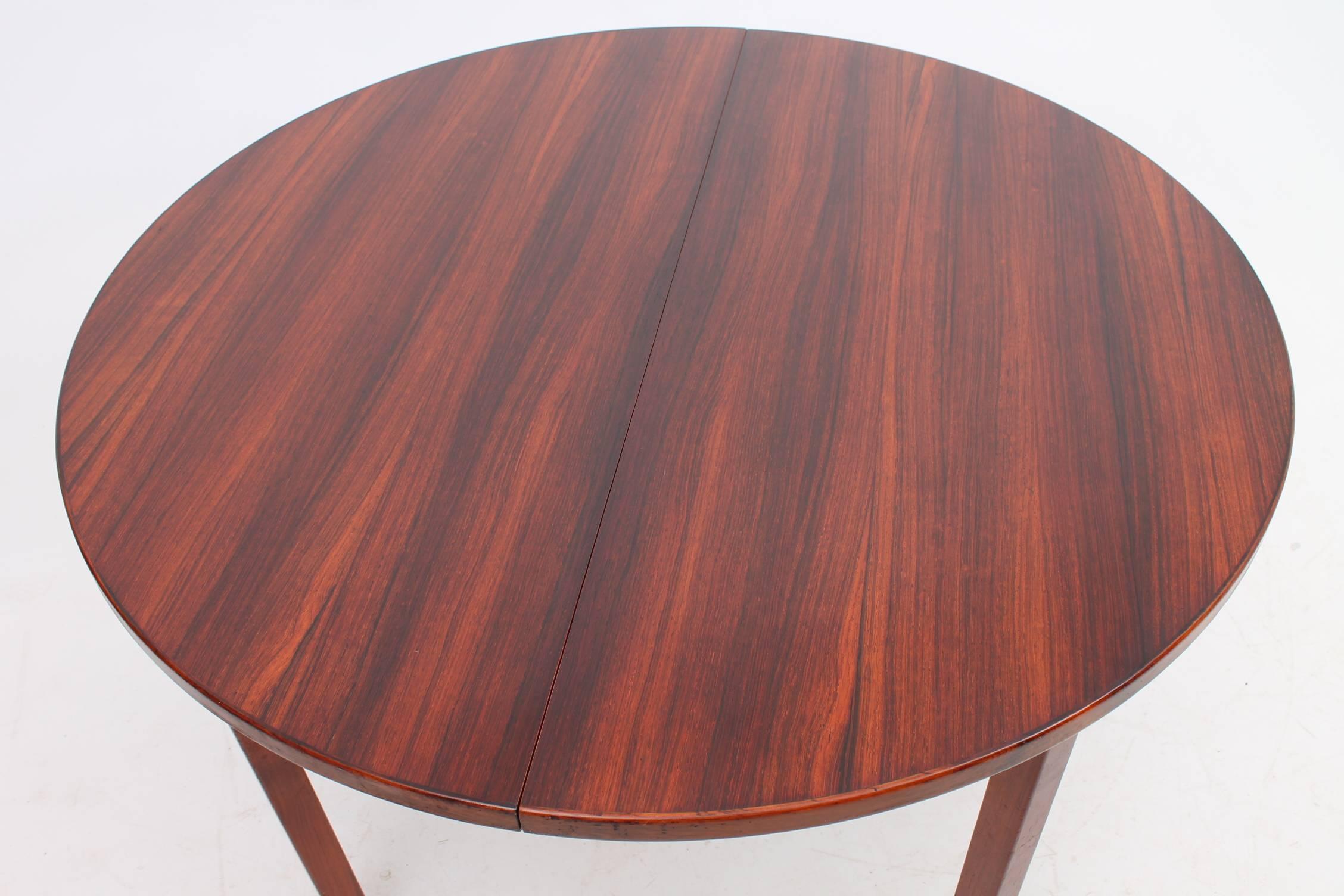 Circular dining table made of rosewood. The leaves of the table fold and hide inside the extending middle. This table has been professionally restored.