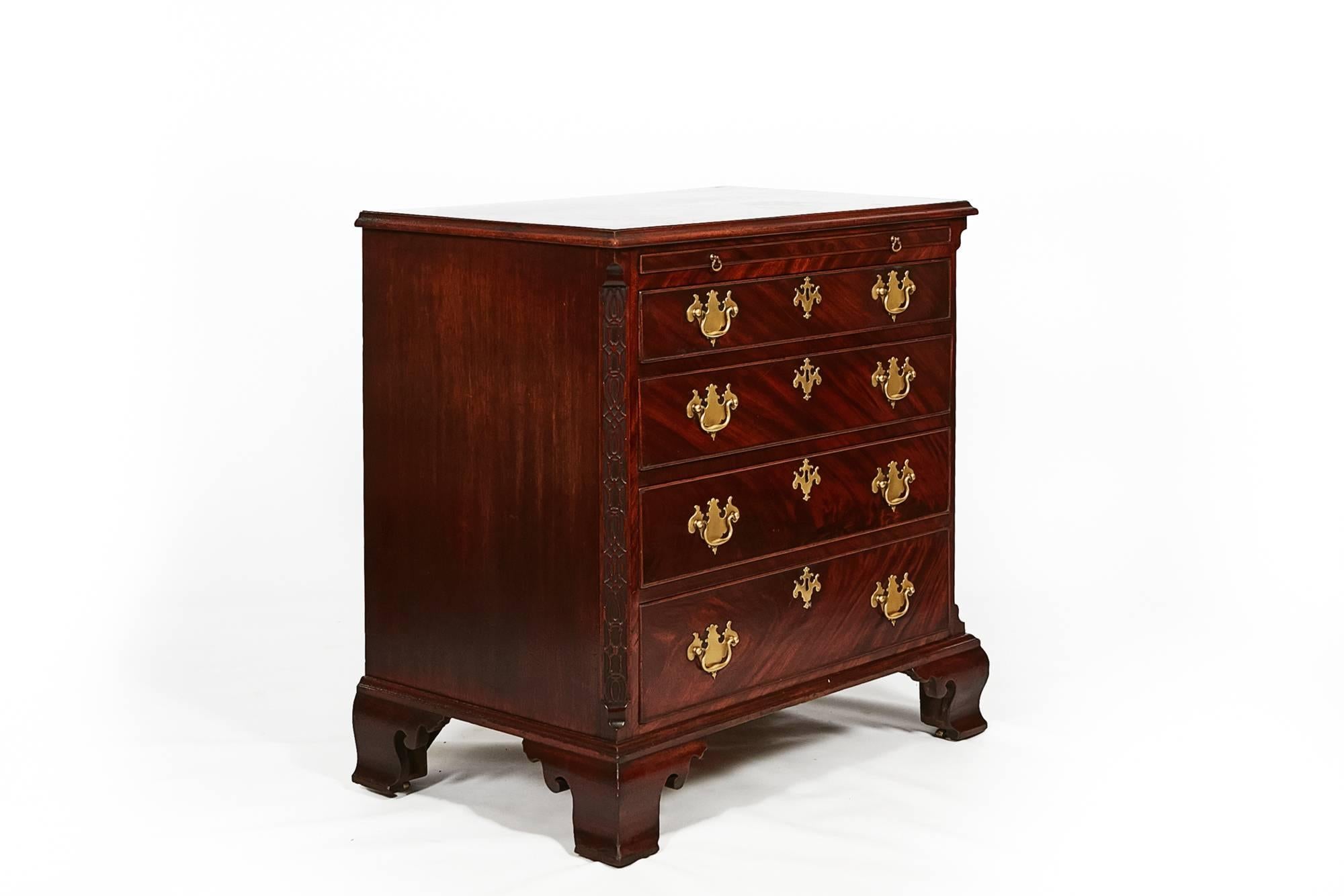 Early 19th century George III bachelor’s flame mahogany four-drawer chest with pull-out writing slide, brass pulls, canted corners with relief carving supported on ogee bracketed feet.