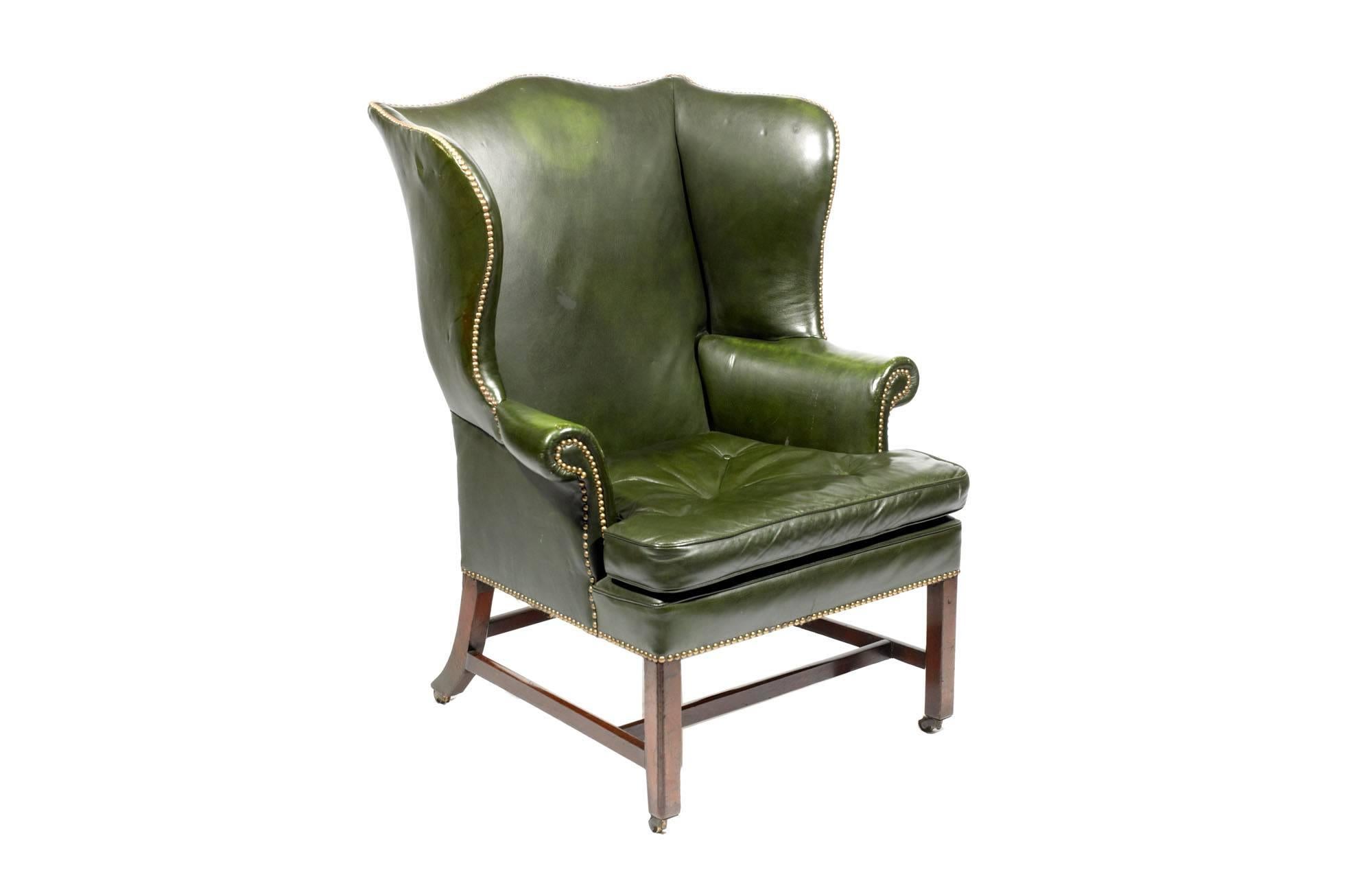 Sillón de orejas georgiano del siglo XVIII, de cuero verde empenachado, sin alas ni brazos con volutas, sobre un cojín suelto y patas cuadradas unidas por una cruceta en H.