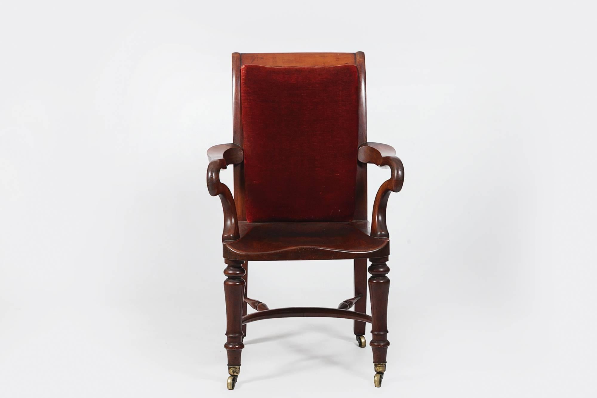 19th century Holland and Son’s Library chair. The solid mahogany frame with a deep saddle seat, padded back and serpentine arms, raised on turned legs, with a bowed crinoline stretcher, terminating on casters.