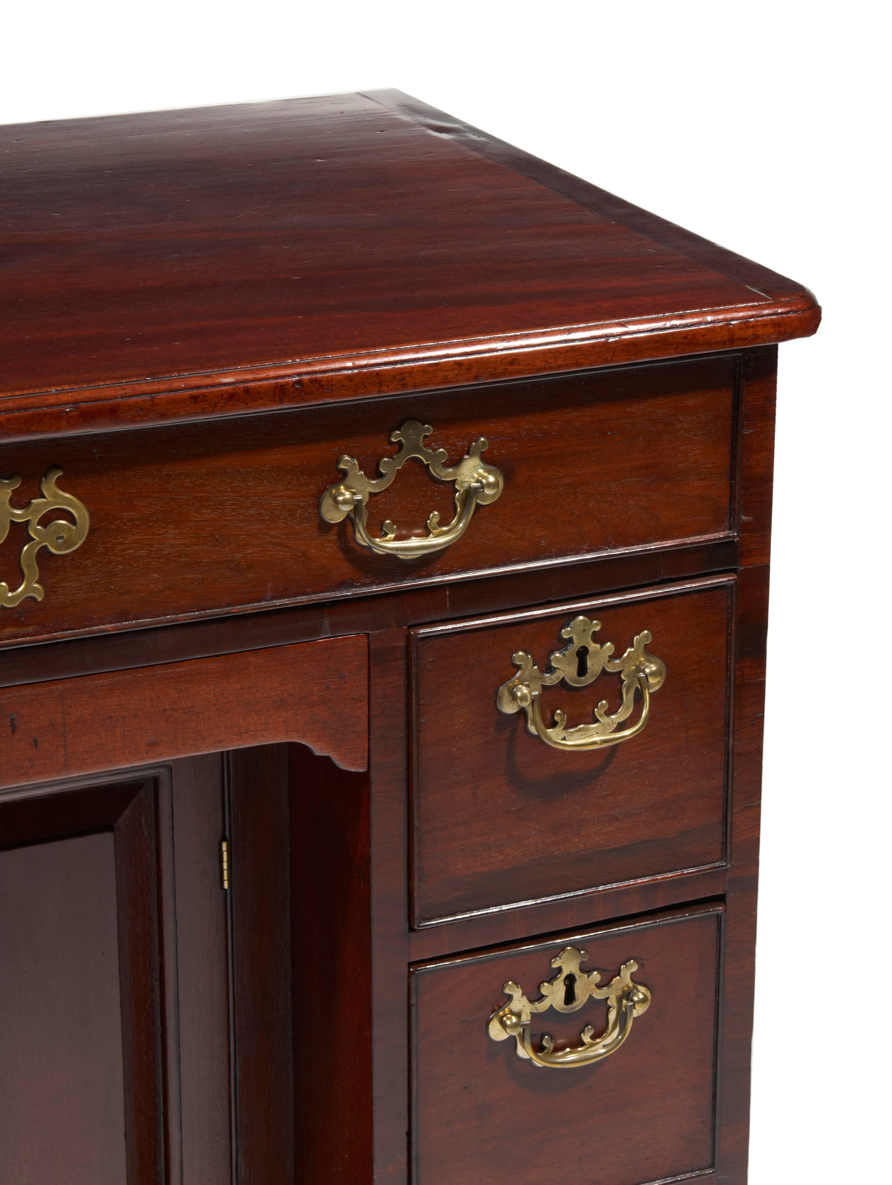 18th century George II mahogany knee hole desk, with one long drawer above central cupboard door flanked by six short drawers raised on bracket feet.