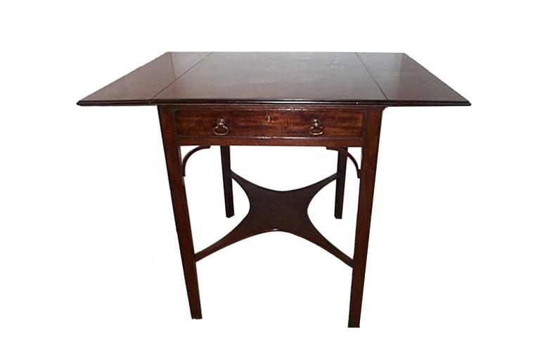 19th century George III mahogany Pembroke table the top with molded edge and drop leaves, with single frieze drawer and carved spandrels raised on straight square section legs with concave stretcher and brass caps and casters.