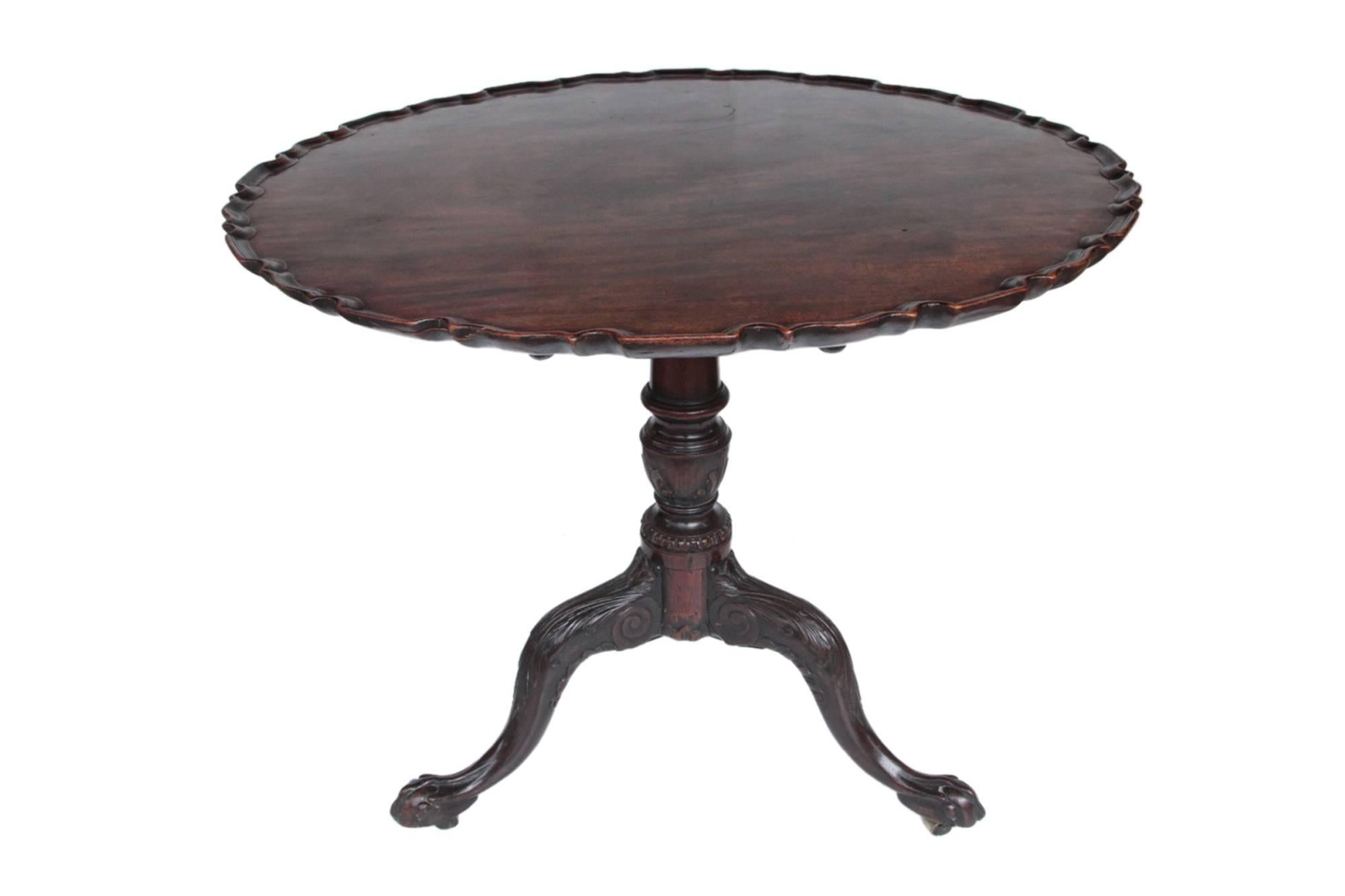 19th century George III mahogany tip-up table. The circular top with carved scallop edge raised on turned pod on carved tripod legs on claw and ball feet.