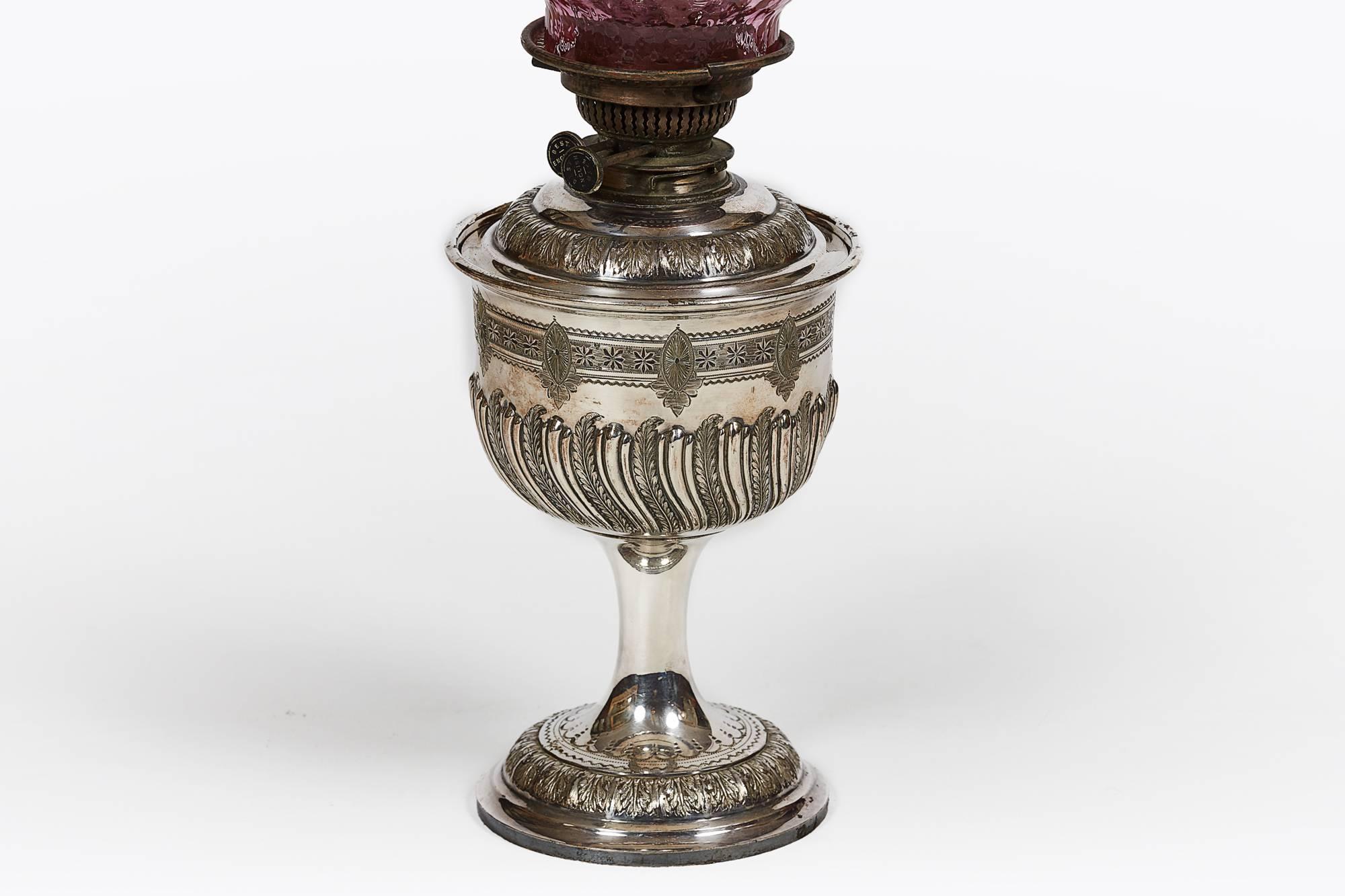 19th century silver and ruby glass oil lamp of classical chalice form with decorative engraving on a circular base with handblown textured ruby glass shade.